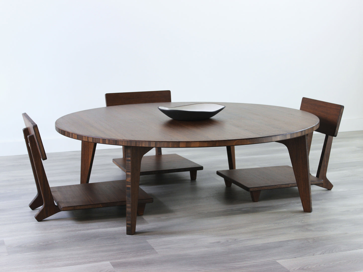Large Circle Low Table set with a walnut bamboo finish and midcentury modern design. Three Floor Chair Comfort are set at the table. Small black pottery vessel placed on table top.
Japandi, minimalist, mid-century, Japanese inspired, modern, contemporary, clean lines, organic design, sustainable bamboo, renewable bamboo, solid bamboo, eco-friendly furniture, natural materials, natural-based finish