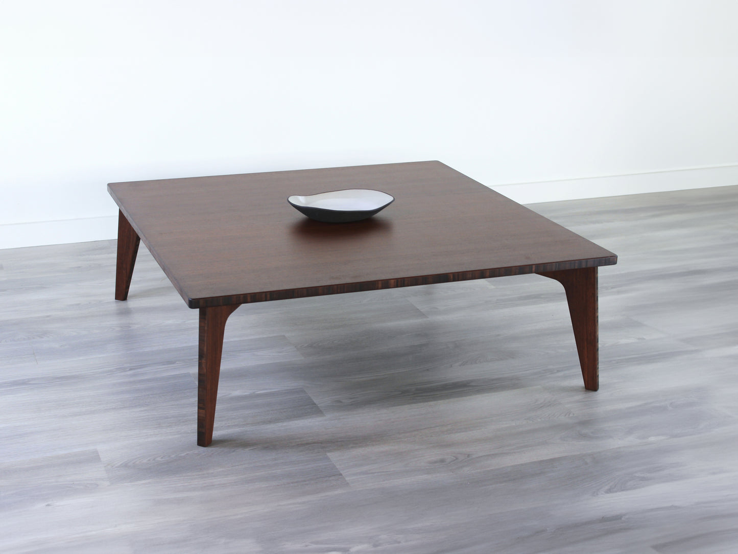 Large square floor table in bamboo with a walnut color finish, featuring a Japandi style design, set on a grey floor with a white background. A small black pottery vessel sets on top.
Square low table
japanese furniture
japanese low table
low coffee table
low dining table
low table
mid century
minimalist
minimalist table
modern
chabudai