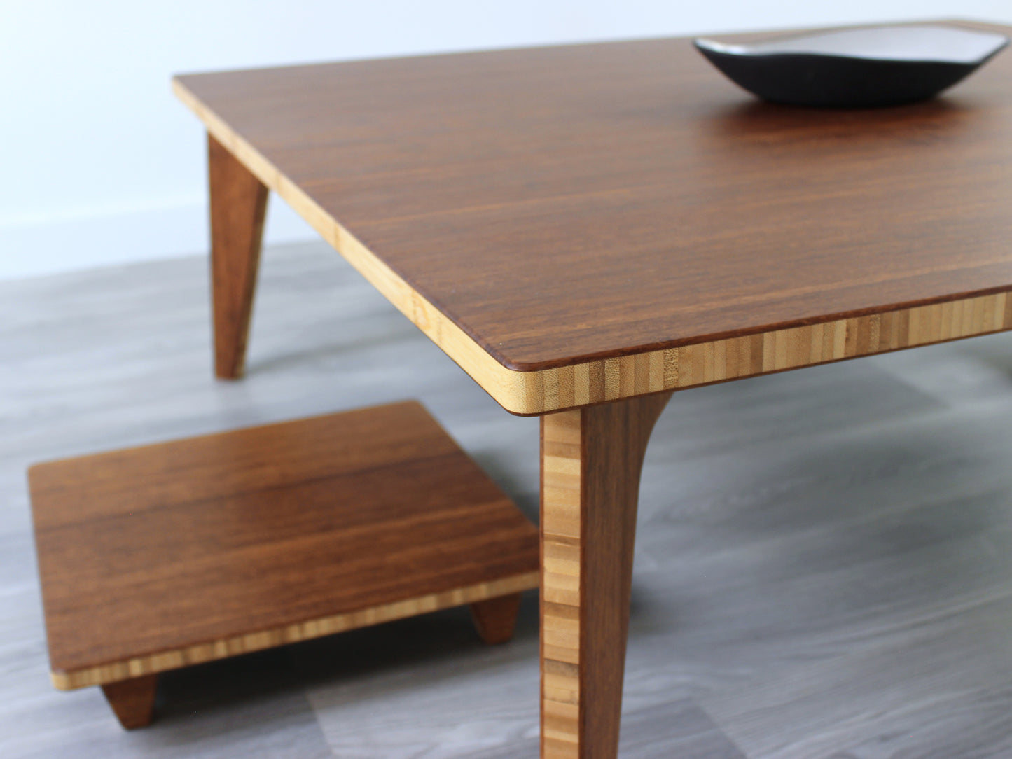 Large square floor table in bamboo with a chestnut color finish, featuring a Japandi style design, set on a grey floor with a white background. A small black pottery vessel sets on top. Floor Chair Posture is set underneath.
Square low table
japanese furniture
japanese low table
low coffee table
low dining table
low table
mid century
minimalist
minimalist table
modern
chabudai
Floor Chair Posture with a grey pillow is set underneath