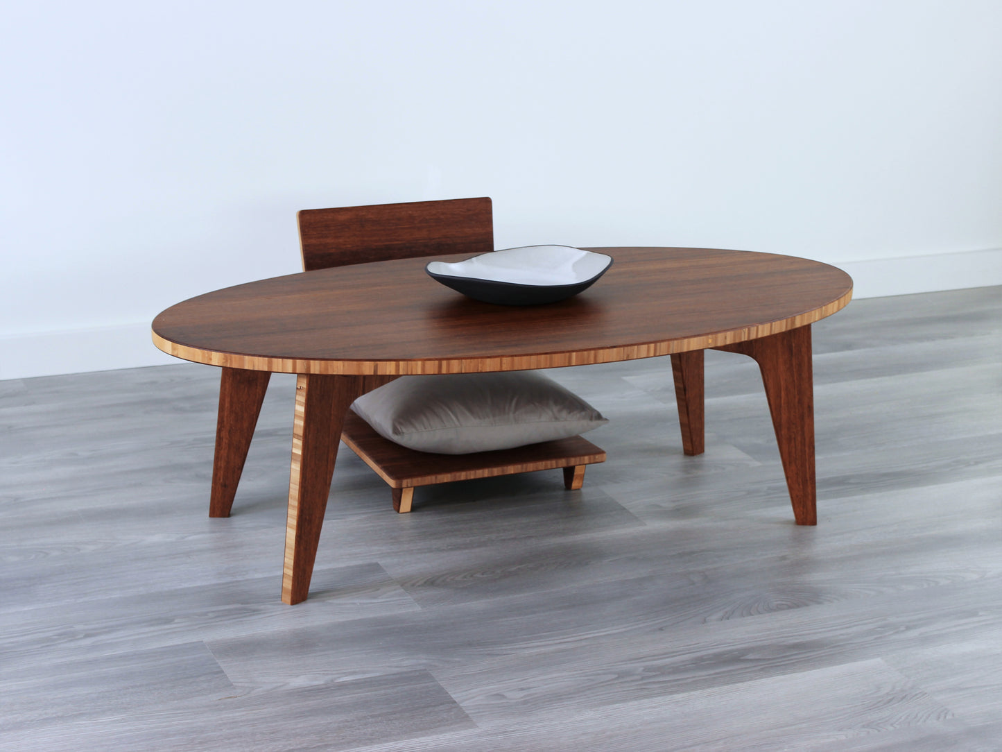 Oval LOW Table set with a chestnut bamboo finish and midcentury modern design. A Floor Chair Comfort with grey pillow are set at the table. Small black pottery vessel placed on table top.
Japandi, minimalist, mid-century, Japanese inspired, modern, contemporary, clean lines, organic design, sustainable bamboo, renewable bamboo, solid bamboo, eco-friendly furniture, natural materials, natural-based finish