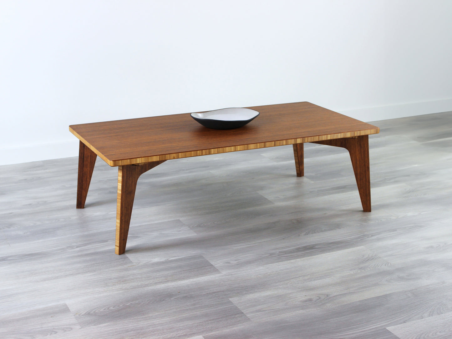A small rectangular low table made of bamboo with a chestnut finish, placed on a grey floor with a white background. A small black pottery vessel is placed on the table top.
japanese furniture
japanese low table
low coffee table
low dining table
low table
mid century
minimalist
minimalist table
modern
chabudai