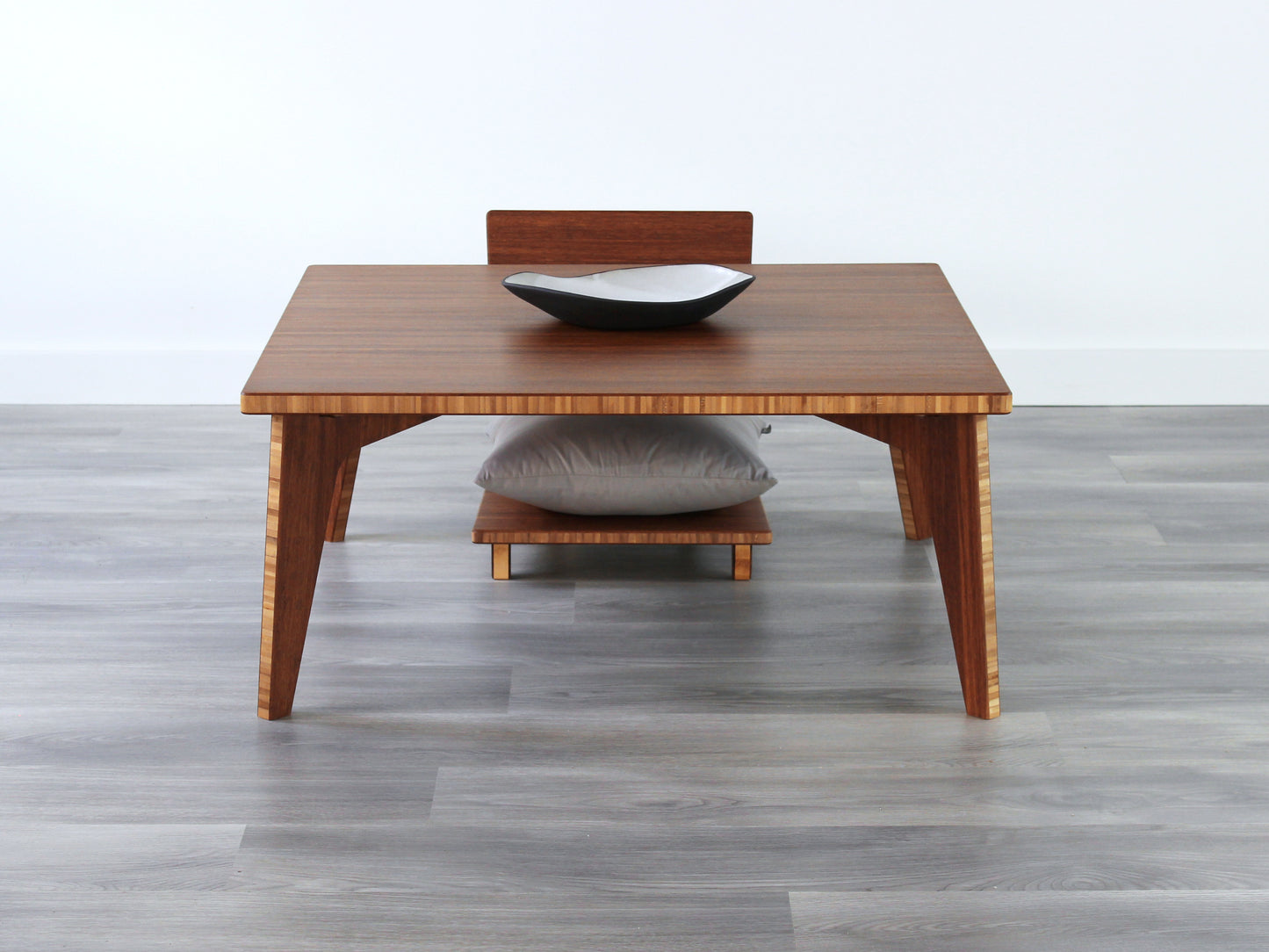Small Square Table Set in chestnut finish. A Floor Chair Comfort with grey pillows are placed below. A small black pottery vessel is placed on top of the table.
sustainable bamboo, renewable bamboo, solid bamboo, eco-friendly furniture, zero-waste, carbon neutral, natural materials, natural-based finish, repairable furniture