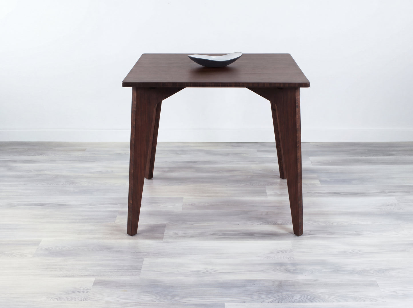 Bamboo dining table with a bowl on a light wooden floor and white wall background