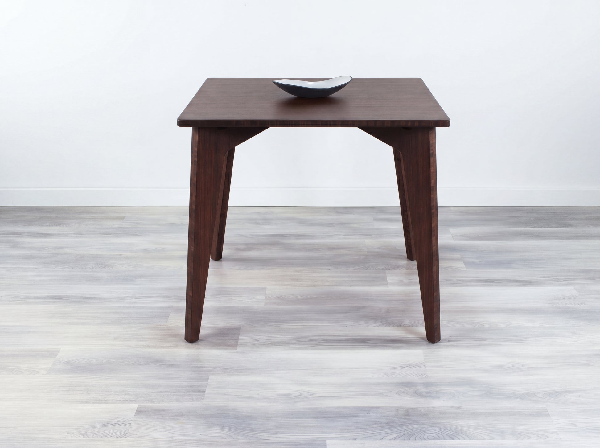 Bamboo dining table with a bowl on a light wooden floor and white wall background
