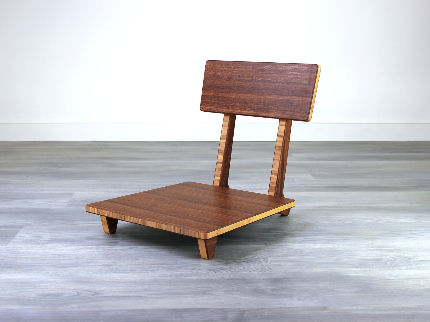 Chestnut bamboo Floor Chair Comfort with a square seat and a vertical supporting structure, displayed on a grey floor and white wall behind. 

floor chair
chabudai
contemporary
low seating 
floor chair with back 
ergonomic 