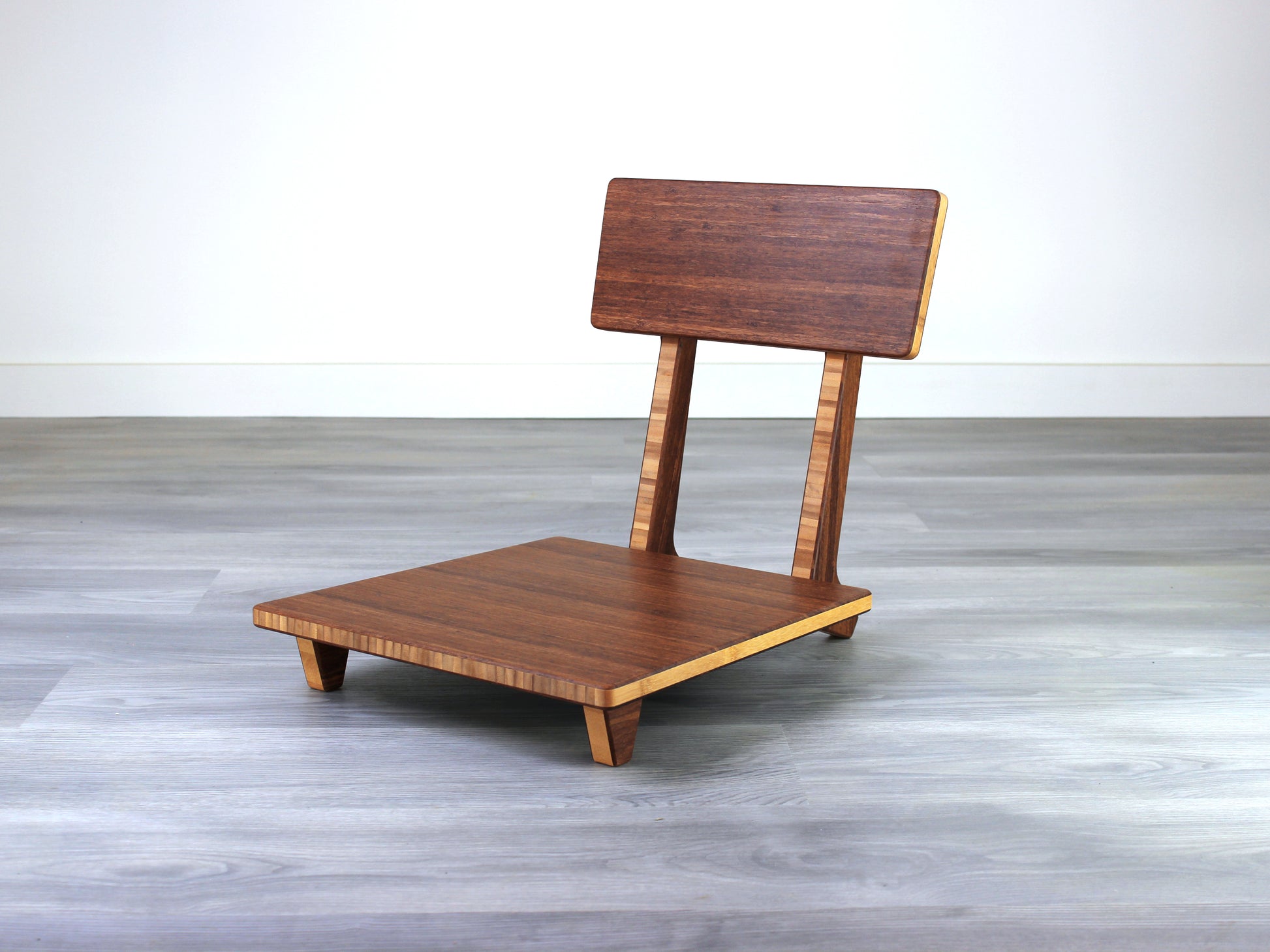 Chestnut bamboo Floor Chair Comfort with a square seat and a vertical supporting structure, displayed on a grey floor and white wall behind. 

floor chair
chabudai
contemporary
low seating 
floor chair with back 
ergonomic 