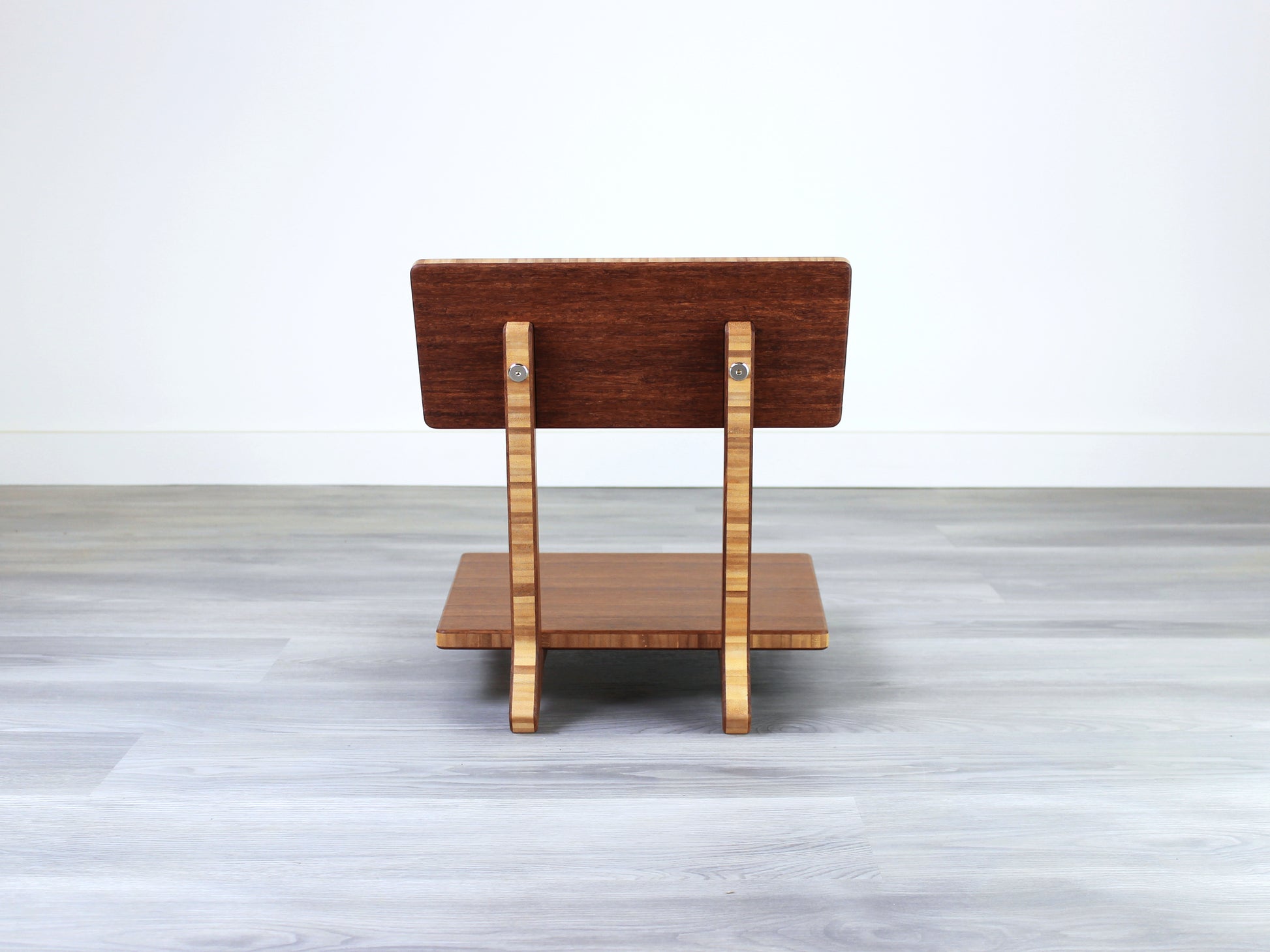 Chestnut bamboo Floor Chair Comfort with a square seat and a vertical supporting structure, displayed on a grey floor and white wall behind. 

floor chair
chabudai
contemporary
low seating 
floor chair with back 
ergonomic 