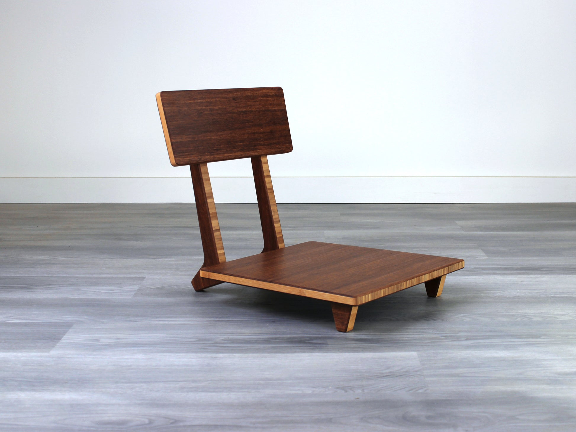 Chestnut bamboo Floor Chair Comfort with a square seat and a vertical supporting structure, displayed on a grey floor and white wall behind. 

floor chair
chabudai
contemporary
low seating 
floor chair with back 
ergonomic 