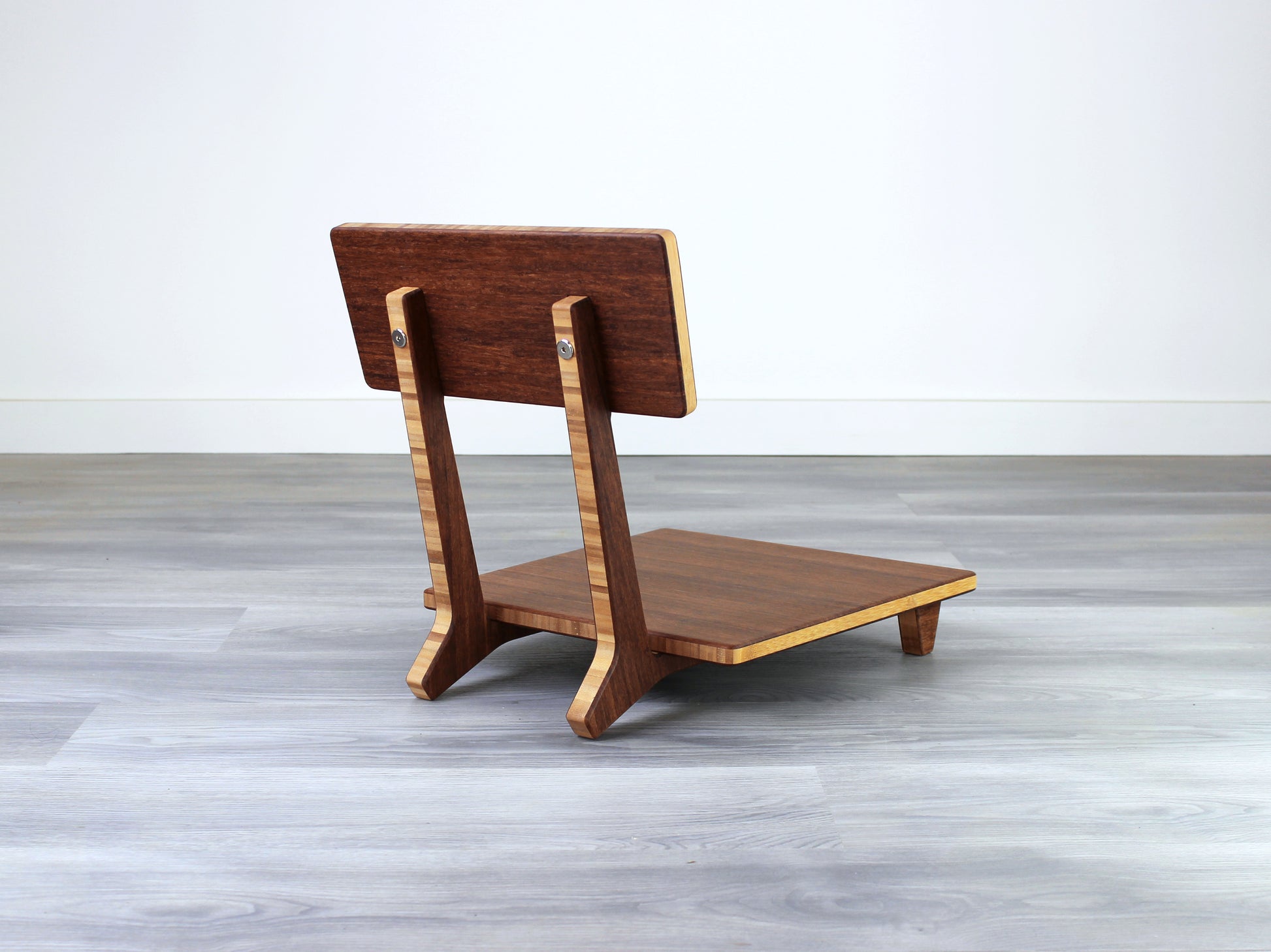 Chestnut bamboo Floor Chair Comfort with a square seat and a vertical supporting structure, displayed on a grey floor and white wall behind. 

floor chair
chabudai
contemporary
low seating 
floor chair with back 
ergonomic 