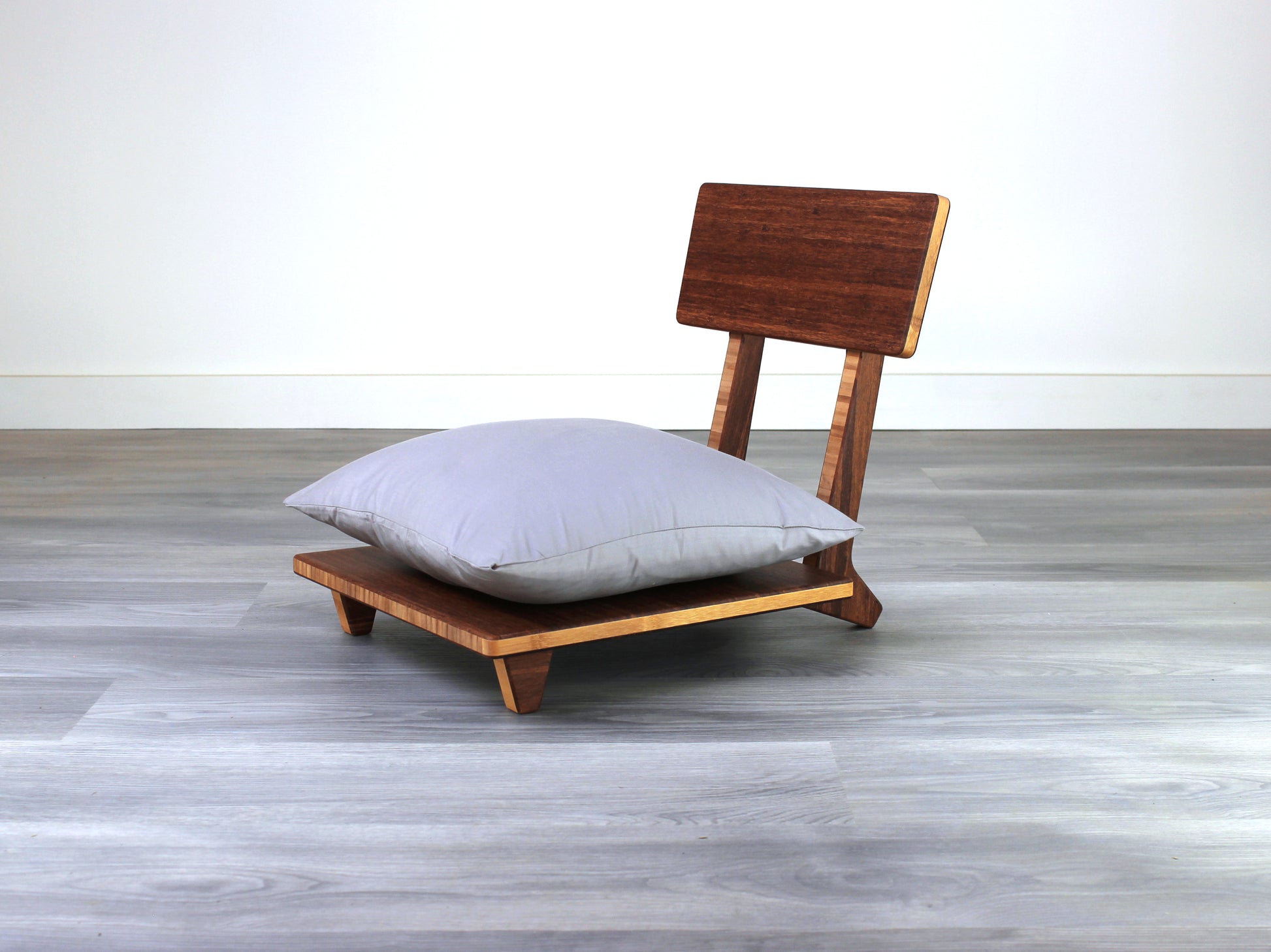Chestnut bamboo Floor Chair Comfort with a square seat and a vertical supporting structure, displayed on a grey floor and white wall behind. 

floor chair
chabudai
contemporary
low seating 
floor chair with back 
ergonomic 
posture support