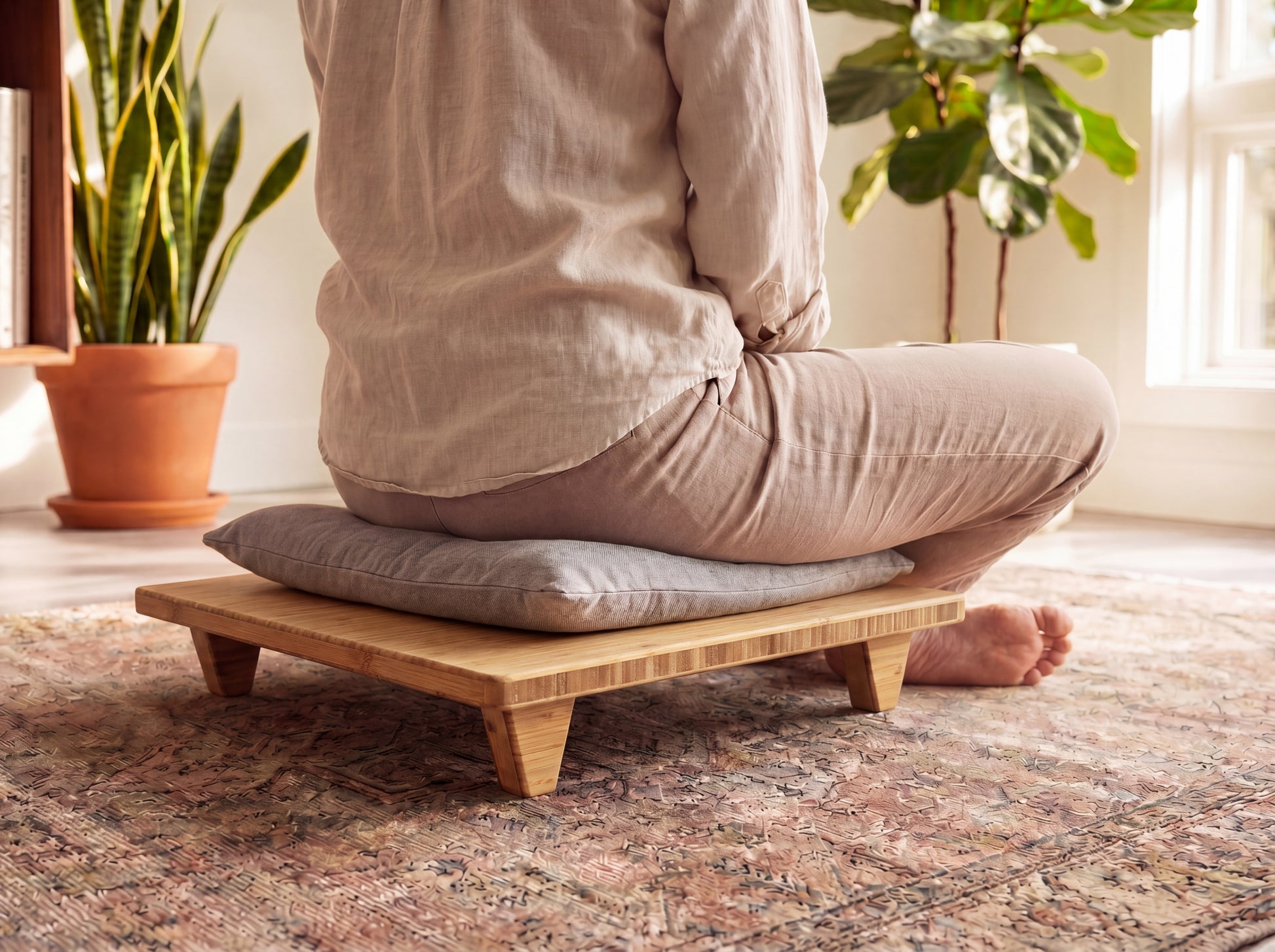 Person sitting cross-legged on a bamboo platform with cushion in a room with plants and a rug.

Meditation Chair 
Japanese Tea Table 
Kotatsu
low chair
posture support 
ergonomic 
minimilist 