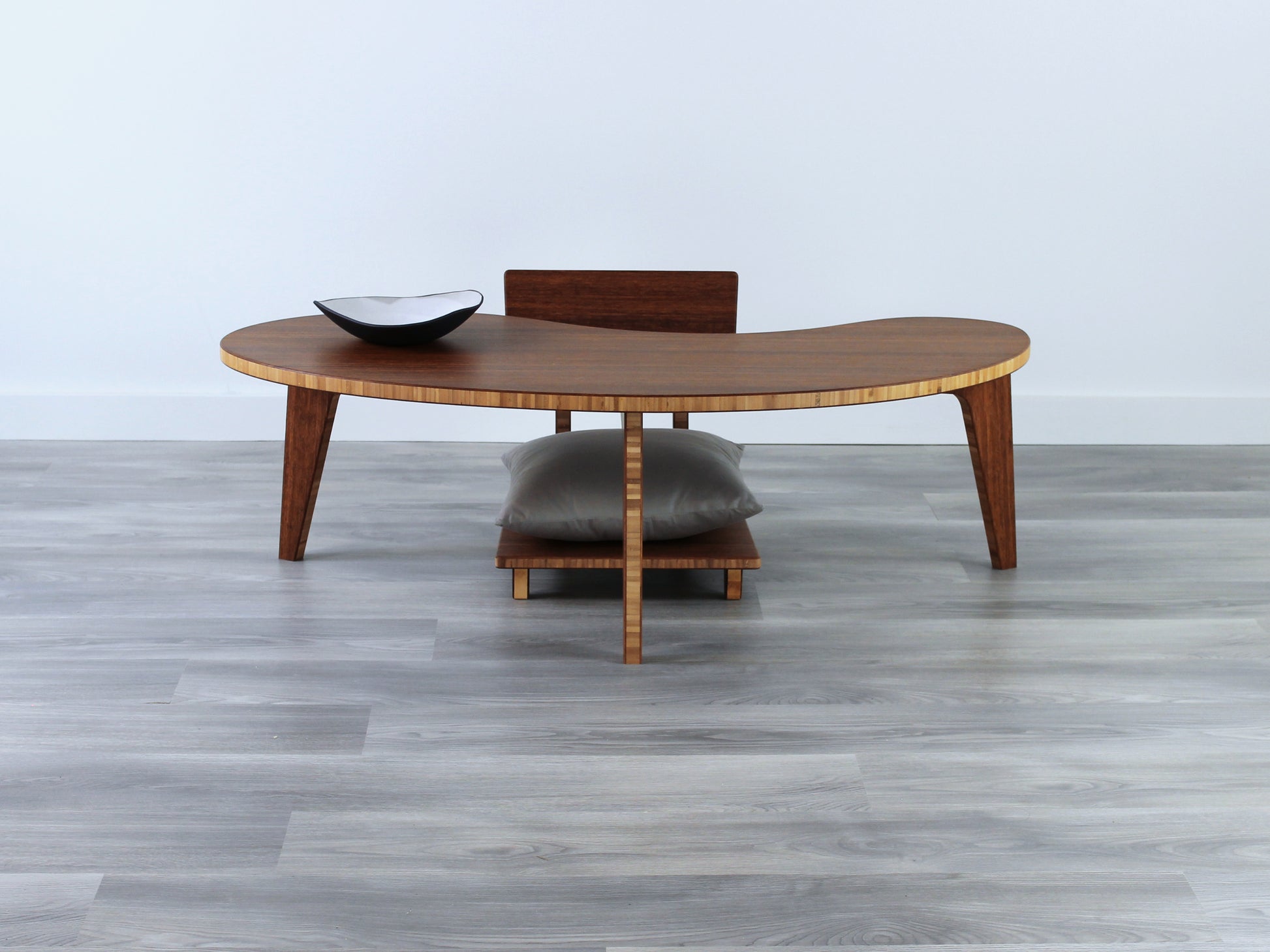 A Kidney LOW Table Set in chestnut bamboo, featuring a small black and white pottery vessel placed on top. Floor Chair Comfort with a grey pillow set underneath. Placed on a Grey flooring with a white background. 

mid century modern low table
midcentury modern coffee table
floor table
japan coffee table
japan furniture
japan table
kidney coffee table 
bamboo low seating