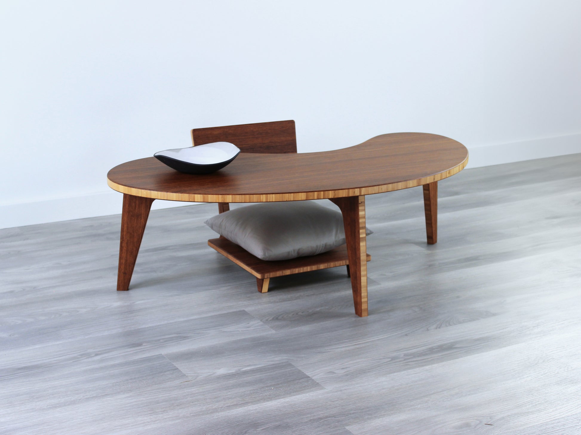 A Kidney LOW Table Set in chestnut bamboo, featuring a small black and white pottery vessel placed on top. Floor Chair Comfort with a grey pillow set underneath. Placed on a Grey flooring with a white background. 

mid century modern low table
midcentury modern coffee table
floor table
japan coffee table
japan furniture
japan table
kidney coffee table 
bamboo low seating