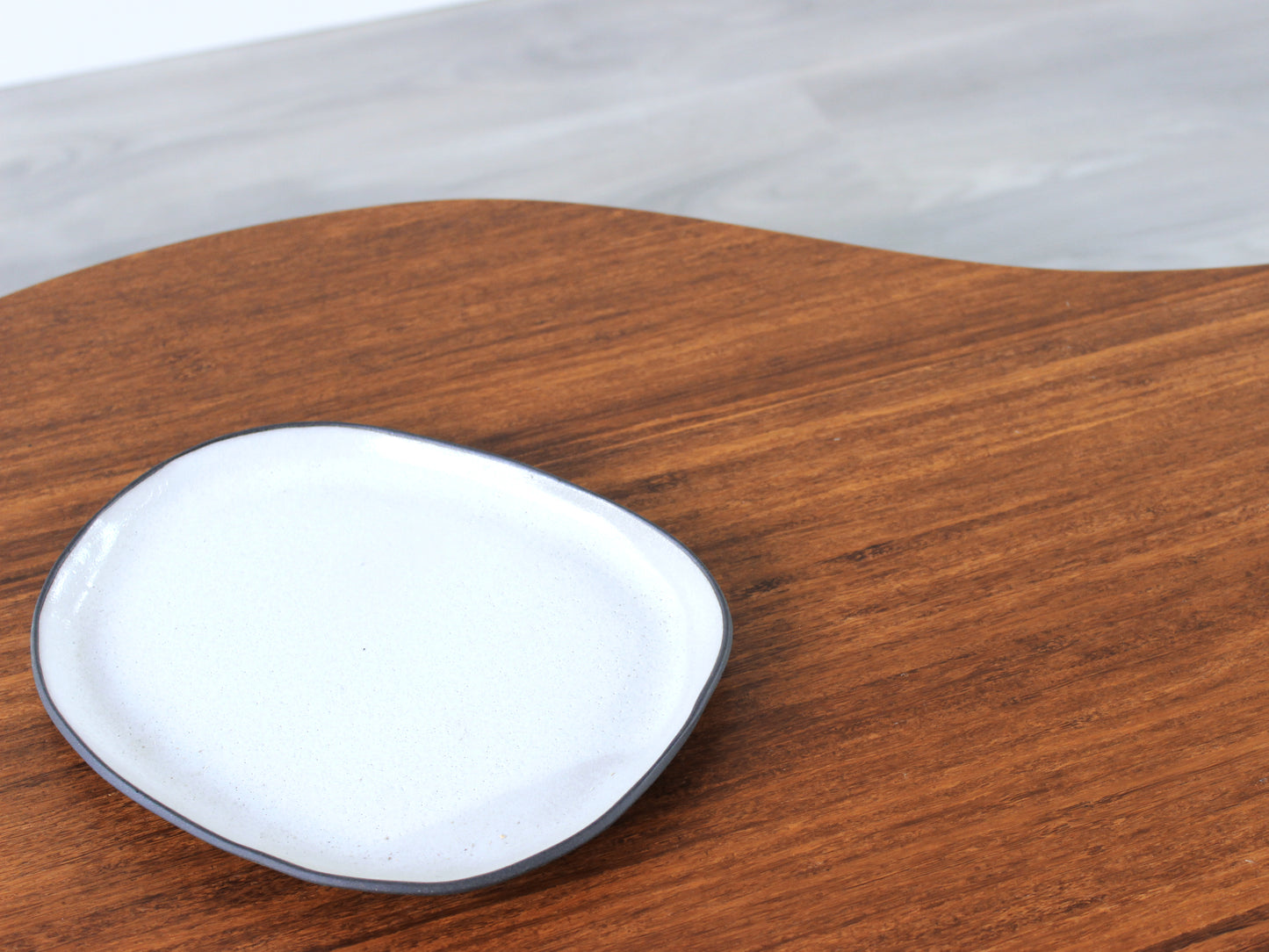 A small kidney-shaped chestnut bamboo table, featuring a small black and white pottery vessel placed on top. Grey flooring with a white background. 

mid century modern low table
midcentury modern coffee table
floor table
japan coffee table
japan furniture
japan table
kidney coffee table 
bamboo low table