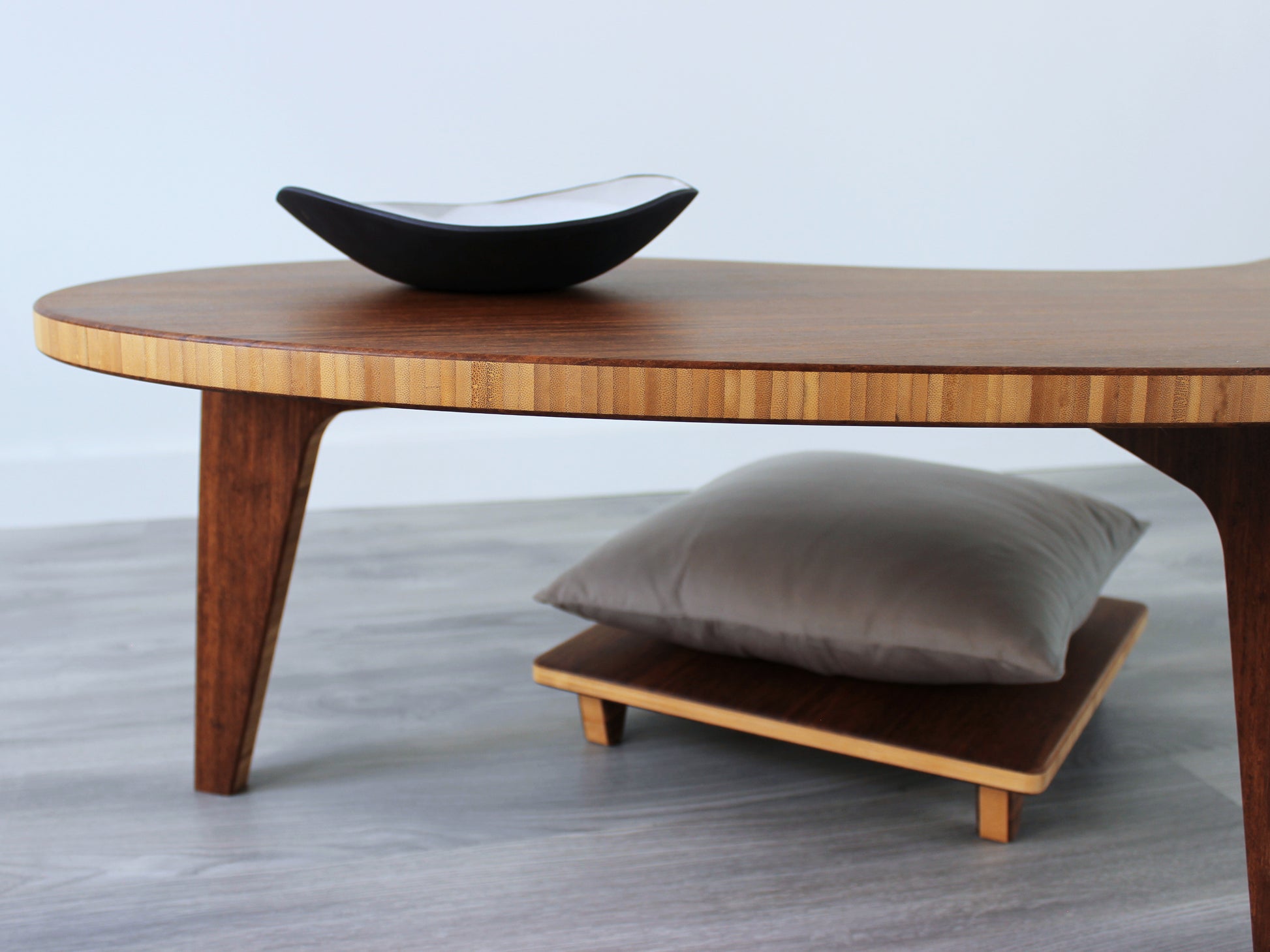 A kidney-shaped chestnut bamboo table, featuring a small black and white pottery vessel placed on top. Grey flooring with a white background. Floor Chair Posture with grey pillow set underneath.

mid century modern low table
midcentury modern coffee table
floor table
japan coffee table
japan furniture
japan table
kidney coffee table 
bamboo low table