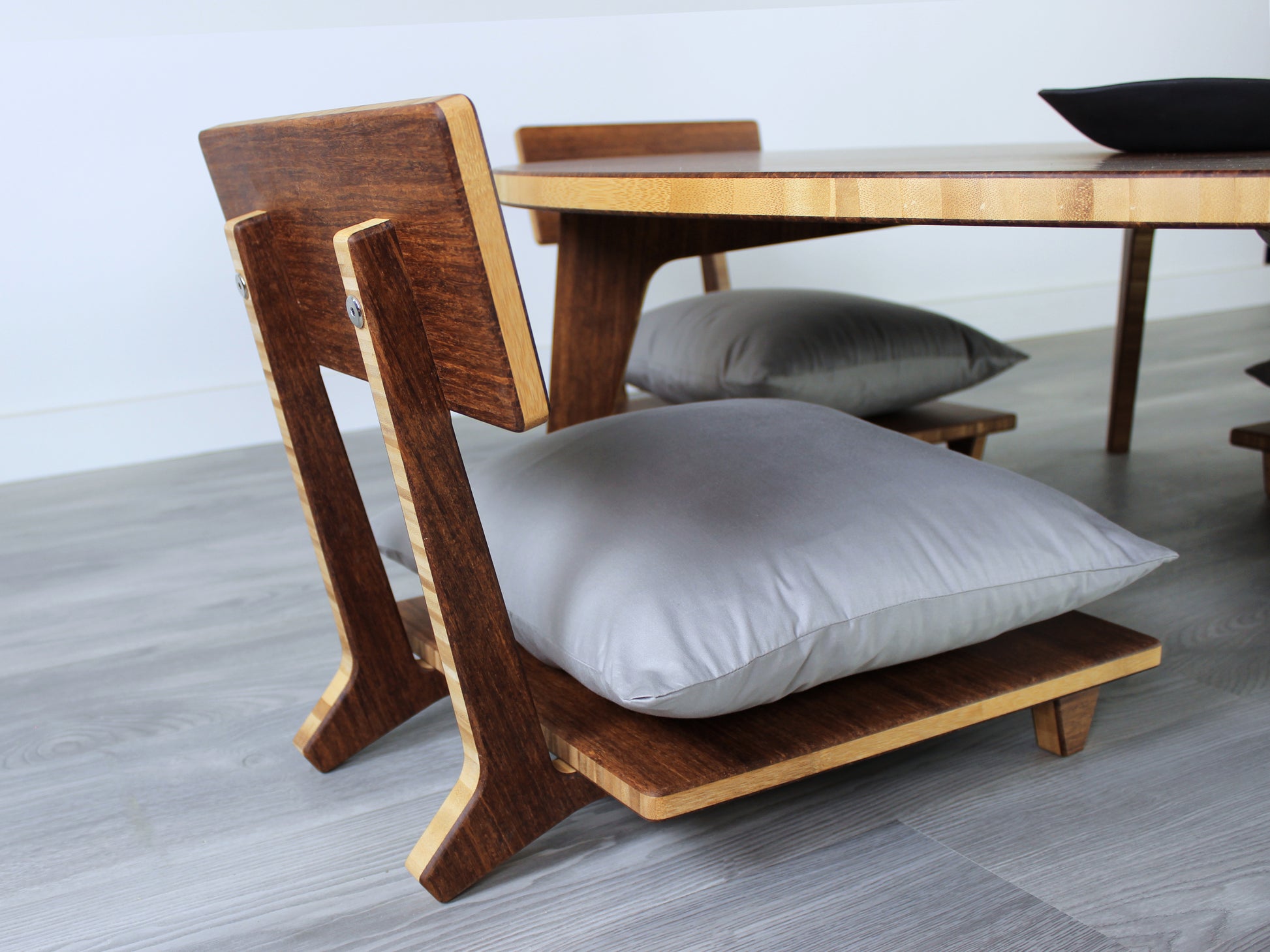 Large Circle Low Table with a chestnut bamboo finish and midcentury modern design. Two Floor Chair Comfort with grey pillows are set at the table. Small black pottery vessel placed on table top. 

Japandi, minimalist, mid-century, Japanese inspired, modern, contemporary, clean lines, organic design, sustainable bamboo, renewable bamboo, solid bamboo, eco-friendly furniture, natural materials, natural-based finish