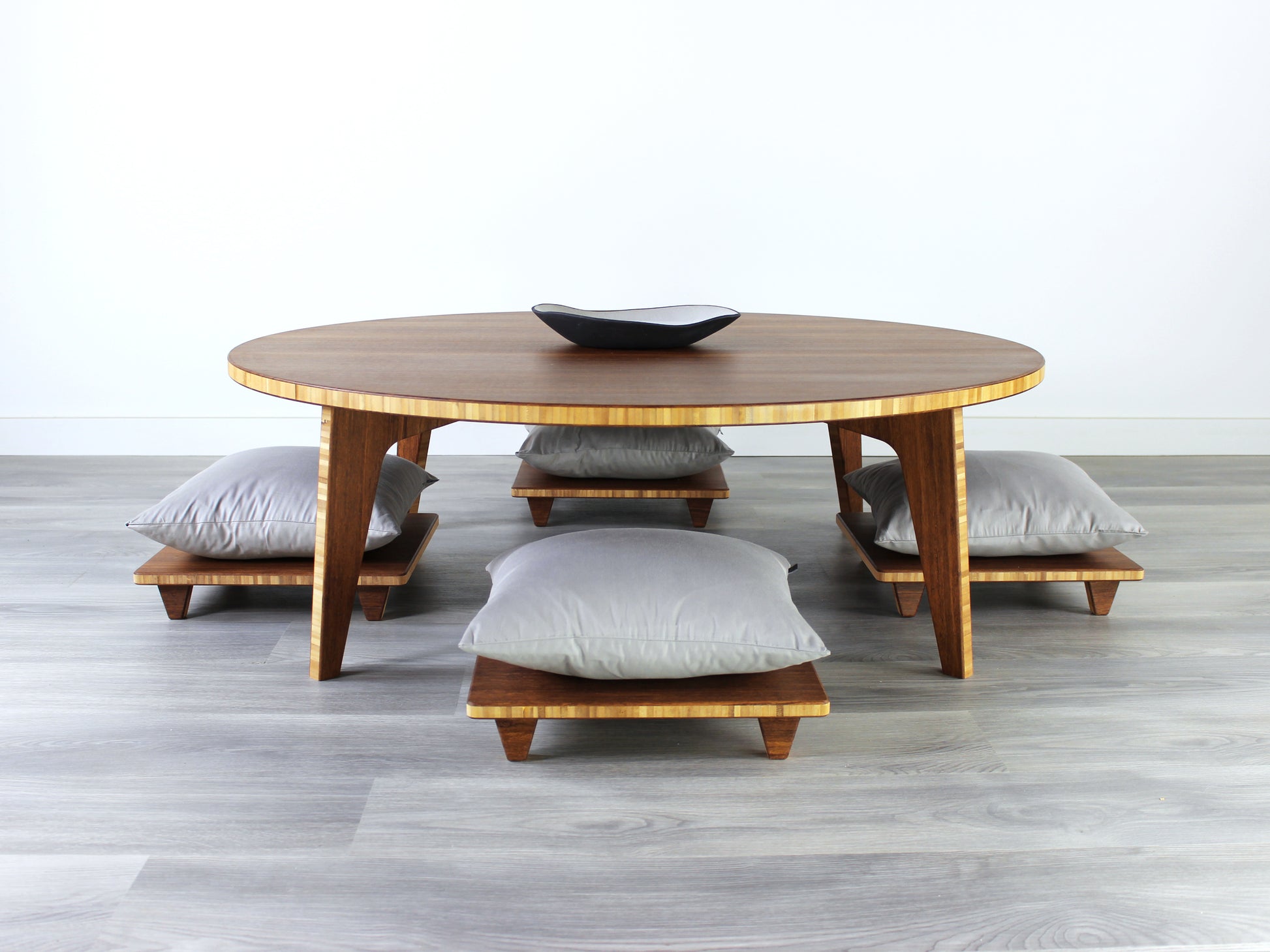 Large Circle Low Table with a chestnut bamboo finish and midcentury modern design. Four Floor Chair Posture with grey pillows are set at the table. Small black pottery vessel placed on table top. 

Japandi, minimalist, mid-century, Japanese inspired, modern, contemporary, clean lines, organic design, sustainable bamboo, renewable bamboo, solid bamboo, eco-friendly furniture, natural materials, natural-based finish