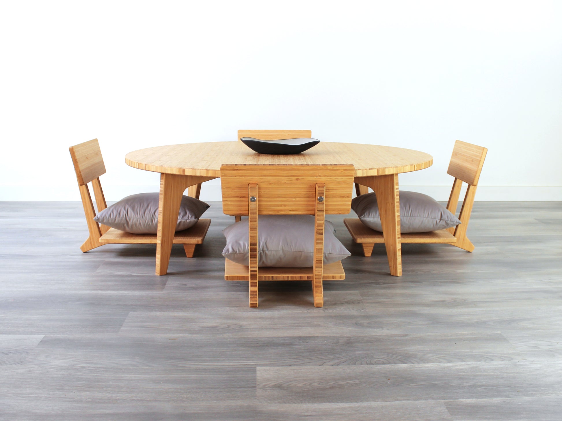 Large Circle Low Table with a natural bamboo finish and midcentury modern design. Four Floor Chair Comfort with grey pillows are set at the table. Small black pottery vessel placed on table top. 

Japandi, minimalist, mid-century, Japanese inspired, modern, contemporary, clean lines, organic design, sustainable bamboo, renewable bamboo, solid bamboo, eco-friendly furniture, natural materials, natural-based finish