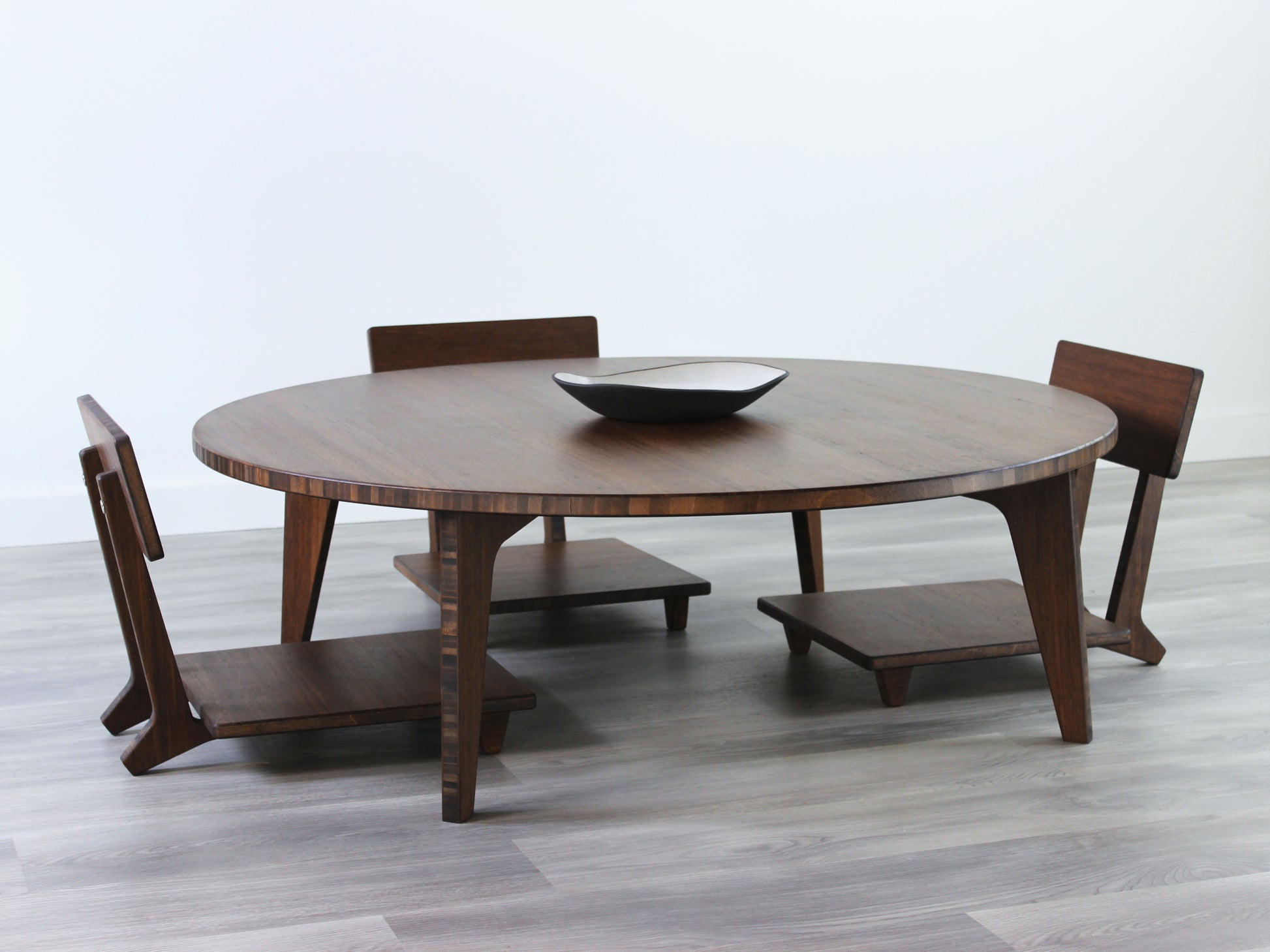 Large Circle Low Table set with a walnut bamboo finish and midcentury modern design. Three Floor Chair Comfort are set at the table. Small black pottery vessel placed on table top. 

Japandi, minimalist, mid-century, Japanese inspired, modern, contemporary, clean lines, organic design, sustainable bamboo, renewable bamboo, solid bamboo, eco-friendly furniture, natural materials, natural-based finish