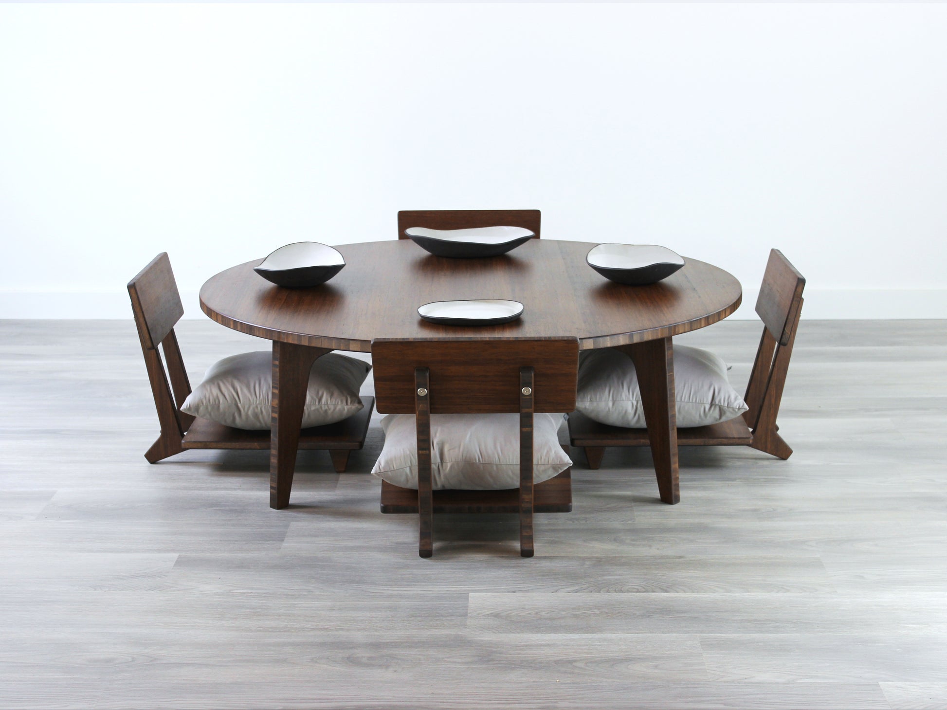 Large Circle Low Table with a walnut bamboo finish and midcentury modern design. Three Floor Chair Comfort with grey pillows are set at the table. Multiple Small black pottery vessels placed on table top. 

Japandi, minimalist, mid-century, Japanese inspired, modern, contemporary, clean lines, organic design, sustainable bamboo, renewable bamboo, solid bamboo, eco-friendly furniture, natural materials, natural-based finish