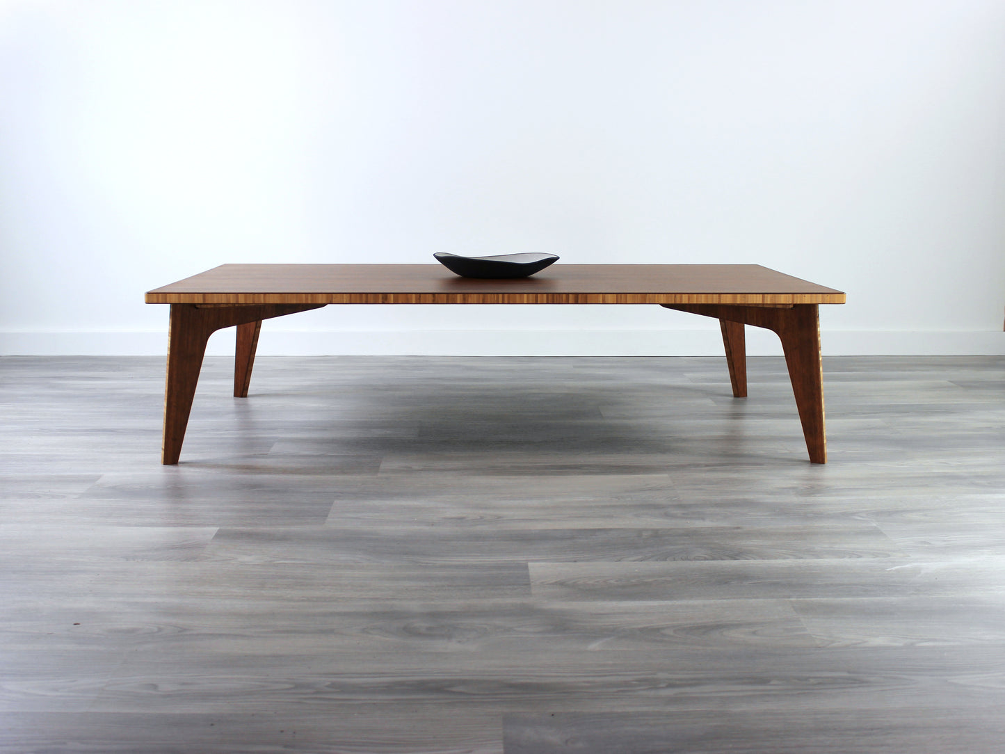 A large rectangular low table made of bamboo with a chestnut finish, placed on a grey floor, designed for multi-functional use in living spaces. A small black pottery vessel set on the table top. 

japanese furniture
japanese low table
low coffee table
low dining table
low table
mid century
minimalist
minimalist table
modern