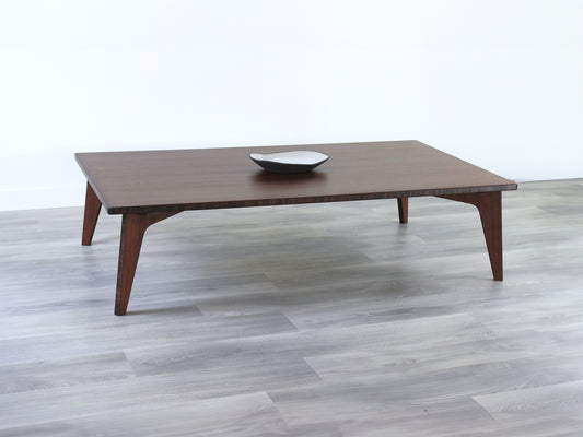 A large rectangular low table made of bamboo with a walnut finish, placed on a grey floor, designed for multi-functional use in living spaces. A small black pottery vessel set on the table top. 

japanese furniture
japanese low table
low coffee table
low dining table
low table
mid century
minimalist
minimalist table
modern