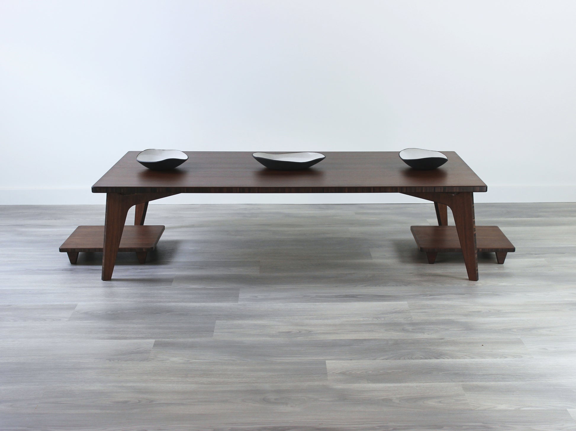 A large rectangular low table made of bamboo with a walnut finish, placed on a grey floor, designed for multi-functional use in living spaces. Three small black pottery vessel set on the table top. Two Floor Chair Posture are set underneath. 

japanese furniture
japanese low table
low coffee table
low dining table
low table
mid century
minimalist
minimalist table
modern
dining table
floor chair
floor cushion
tatami
kotatsu
