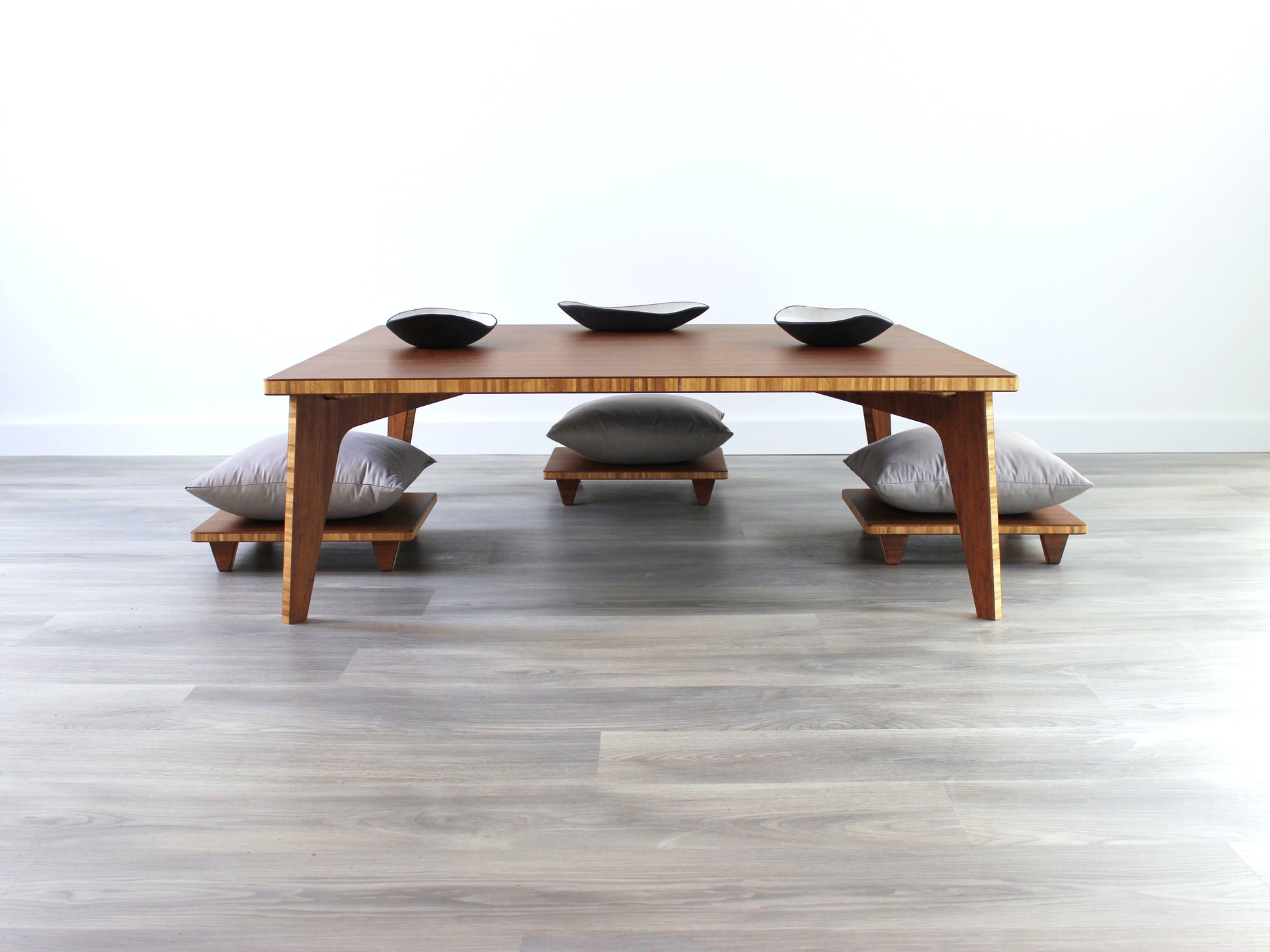 Large Square Low Table with a chestnut bamboo finish and midcentury modern design. Three Floor Chair Posture with grey pillows are set at the table. Small black pottery vessel placed on table top. 

Japandi, minimalist, mid-century, Japanese inspired, modern, contemporary, clean lines, organic design, sustainable bamboo, renewable bamboo, solid bamboo, eco-friendly furniture, natural materials, natural-based finish