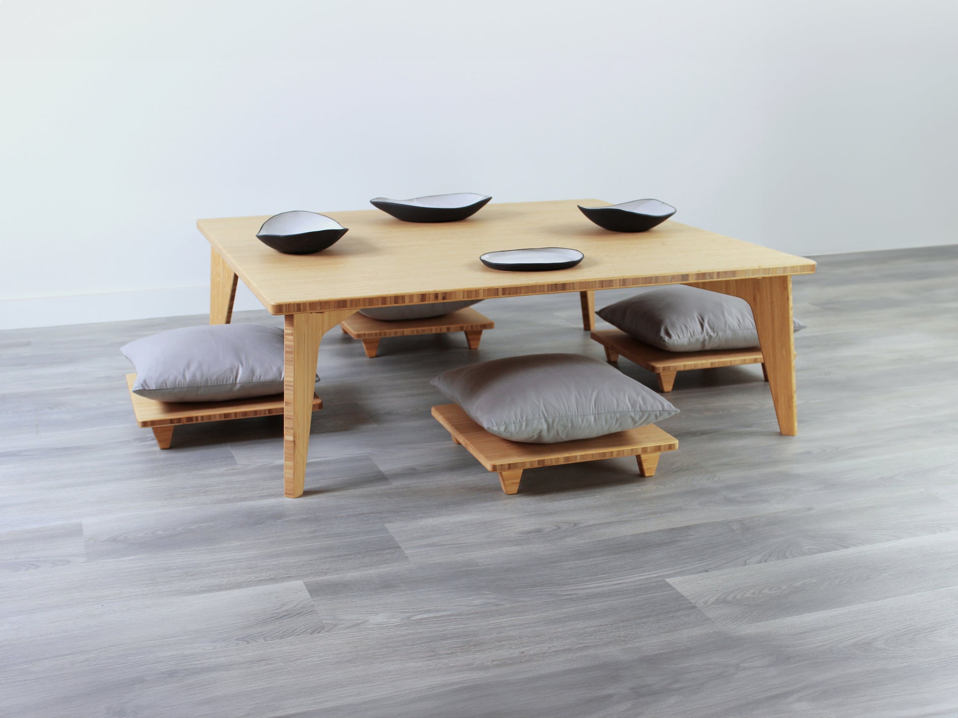 Large Square Low Table with a natural bamboo finish and midcentury modern design. Four Floor Chair Posture with grey pillows are set at the table. Small black pottery vessels placed on table top. 

Japandi, minimalist, mid-century, Japanese inspired, modern, contemporary, clean lines, organic design, sustainable bamboo, renewable bamboo, solid bamboo, eco-friendly furniture, natural materials, natural-based finish
