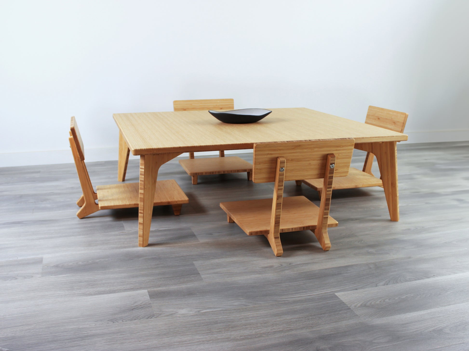 Large Square Low Table with a natural bamboo finish and midcentury modern design. Four Floor Chair Comfort with grey pillows are set at the table. Small black pottery vessel placed on table top. 

Japandi, minimalist, mid-century, Japanese inspired, modern, contemporary, clean lines, organic design, sustainable bamboo, renewable bamboo, solid bamboo, eco-friendly furniture, natural materials, natural-based finish