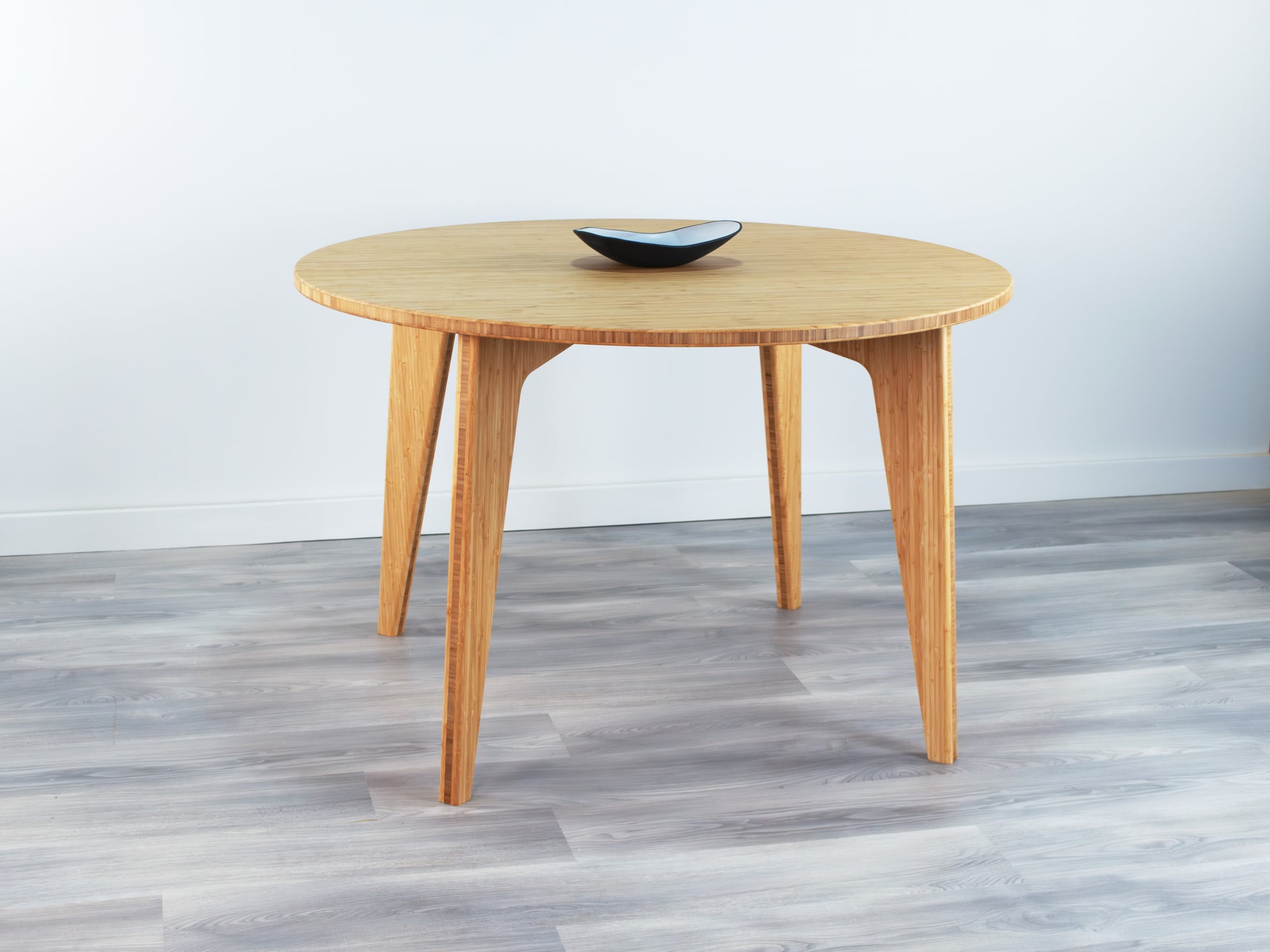 Bamboo dining table with a black bowl on a gray floor and light gray wall background