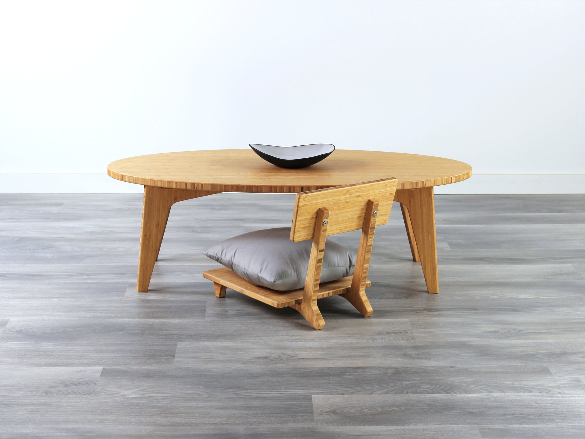 Oval LOW Table set with a natural bamboo finish and midcentury modern design. A Floor Chair Posture with grey pillow are set at the table. Small black pottery vessel placed on table top. 

Japandi, minimalist, mid-century, Japanese inspired, modern, contemporary, clean lines, organic design, sustainable bamboo, renewable bamboo, solid bamboo, eco-friendly furniture, natural materials, natural-based finish