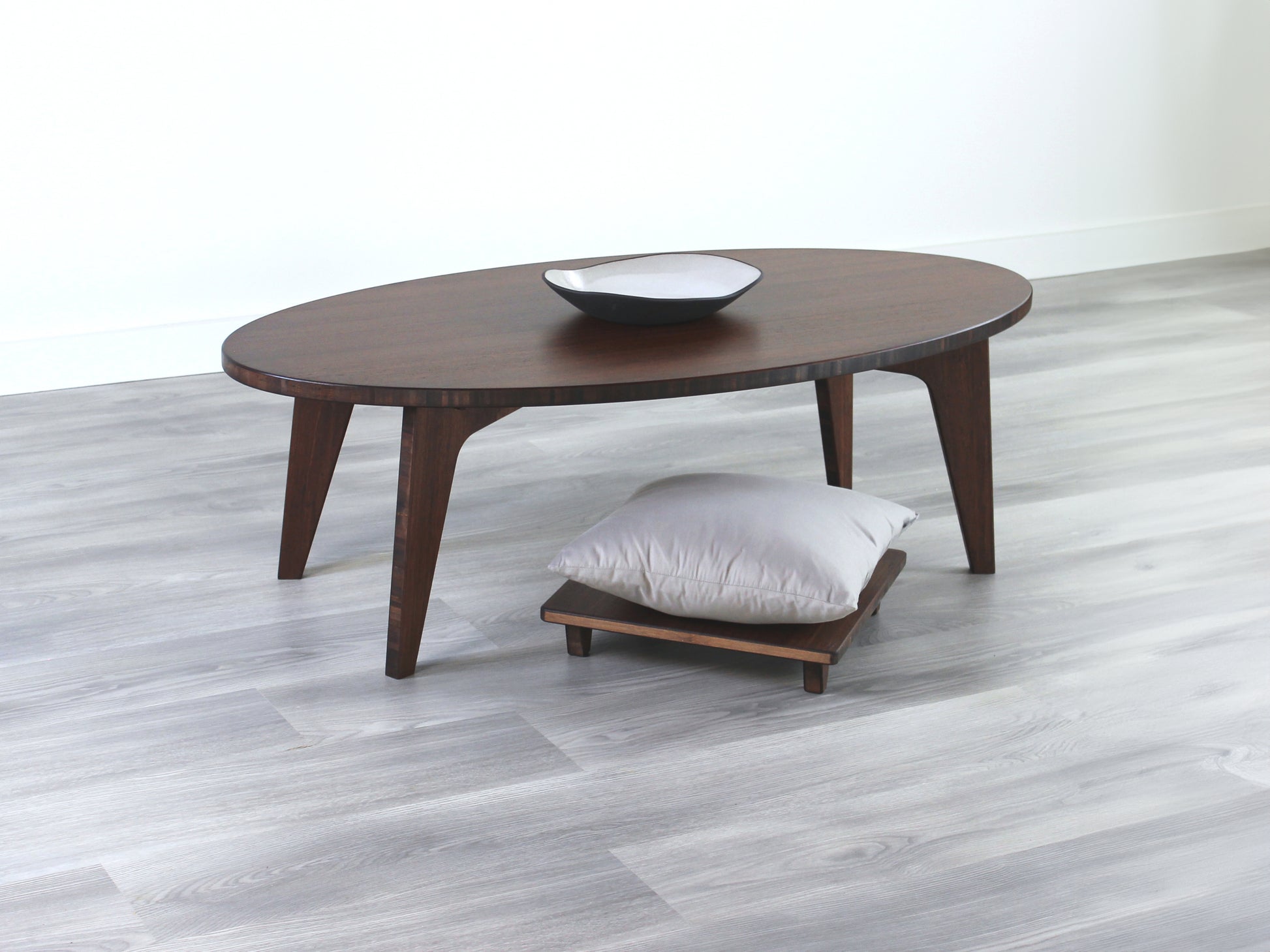 Oval LOW Table set with a walnut bamboo finish and midcentury modern design. A Floor Chair Posture with grey pillow are set at the table. Small black pottery vessel placed on table top. 

Japandi, minimalist, mid-century, Japanese inspired, modern, contemporary, clean lines, organic design, sustainable bamboo, renewable bamboo, solid bamboo, eco-friendly furniture, natural materials, natural-based finish