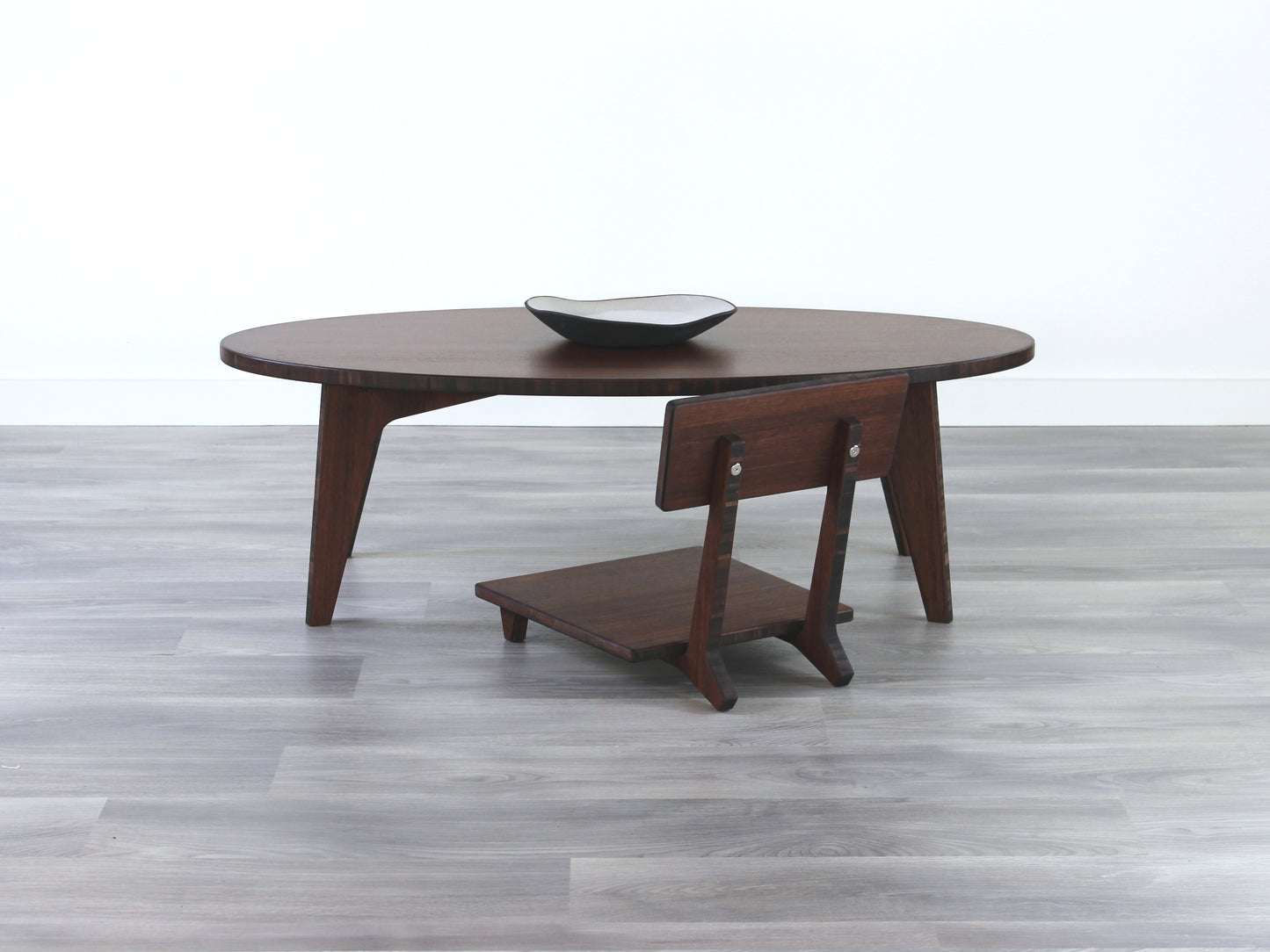 Oval LOW Table set with a walnut bamboo finish and midcentury modern design. A Floor Chair Comfort set at the table. Small black pottery vessel placed on table top. 

Japandi, minimalist, mid-century, Japanese inspired, modern, contemporary, clean lines, organic design, sustainable bamboo, renewable bamboo, solid bamboo, eco-friendly furniture, natural materials, natural-based finish