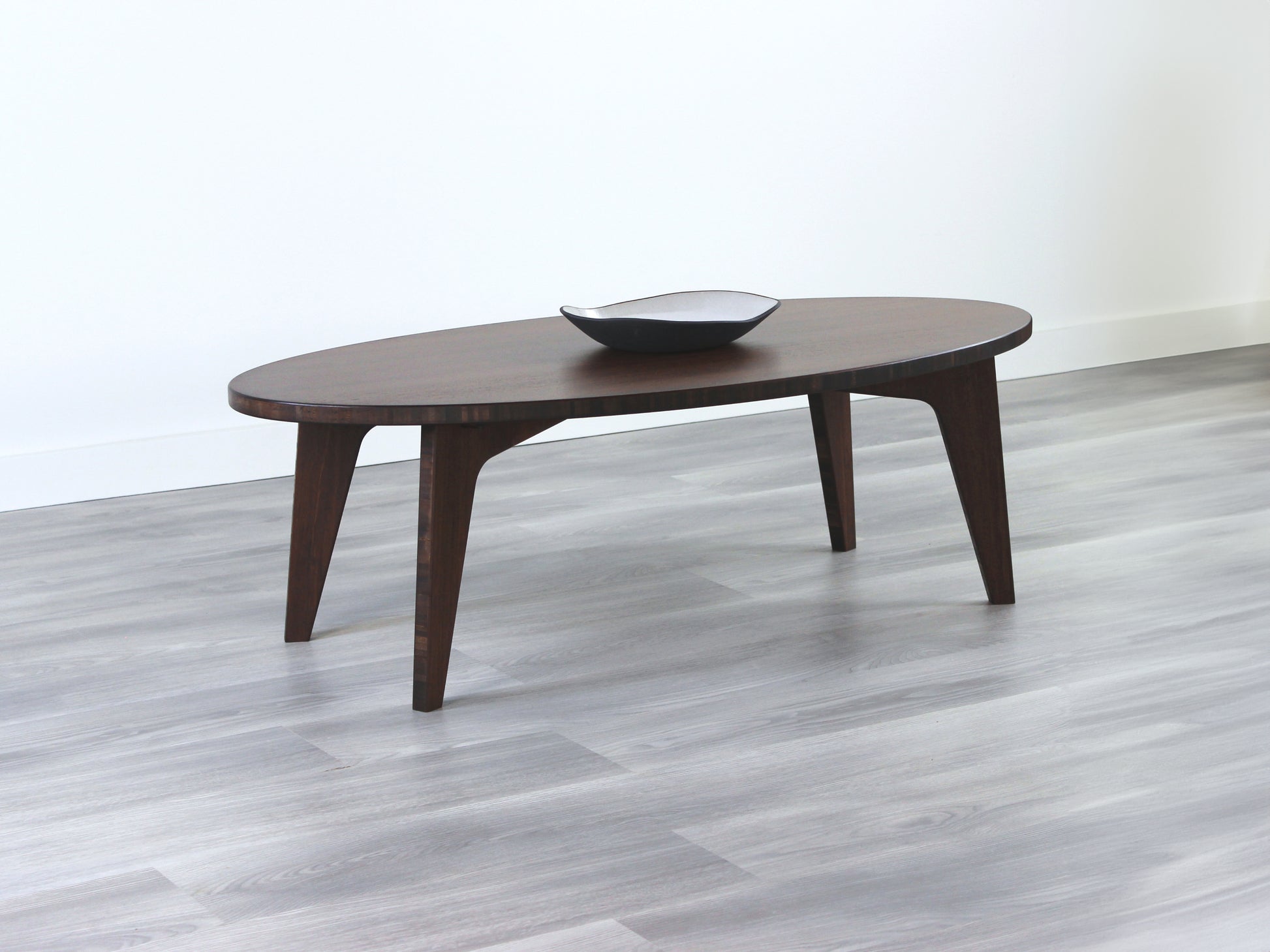 Oval bamboo table with a walnut color finish, featuring a Japandi style design, set on a grey floor with a white background. A small black pottery vessel is placed on the table top. 

mid century modern low table
midcentury modern coffee table
floor table
japan coffee table
japan furniture
japan table
bamboo low table
