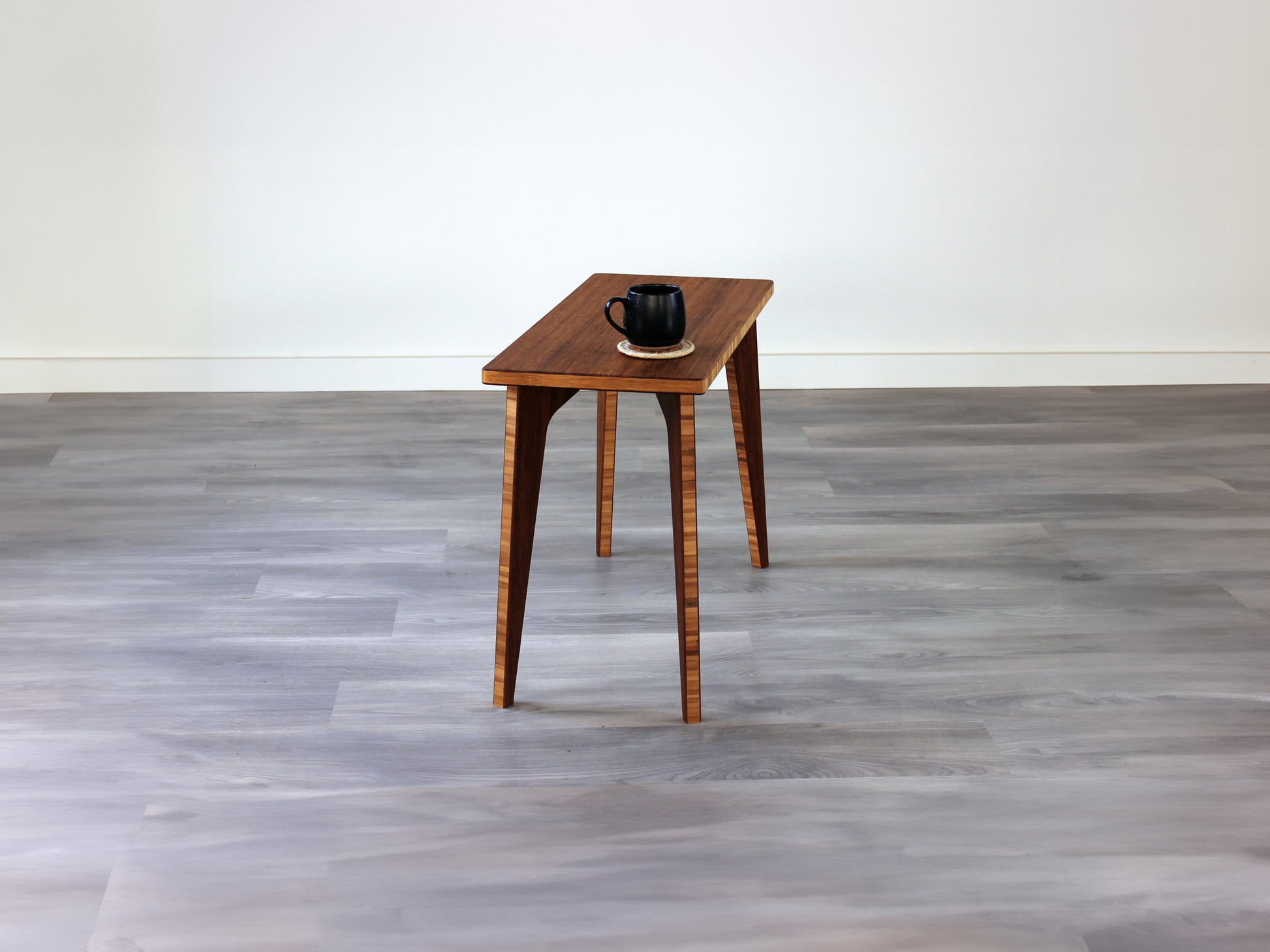 A rectangular side table with a chestnut finish bamboo top and legs, placed on a grey floor, with a white background. Black cup on top of the table.
mid century
minimalist
chabudai
coffee table
side table

