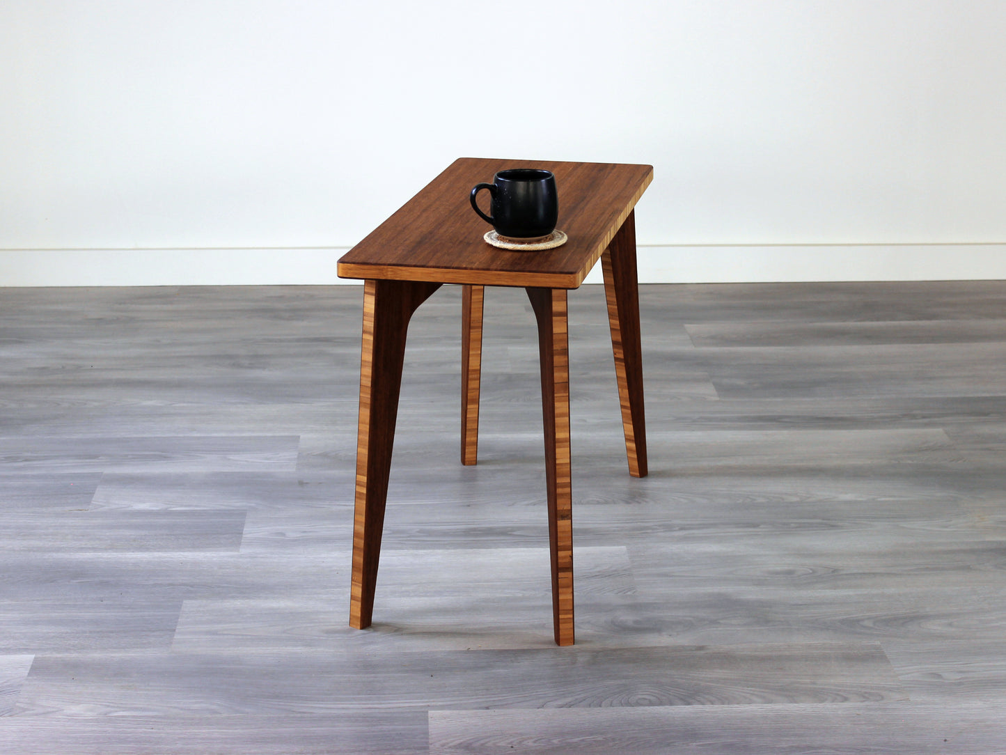 A rectangular side table with a chestnut finish bamboo top and legs, placed on a grey floor, with a white background. Black cup on top of the table.
mid century
minimalist
chabudai
coffee table
side table