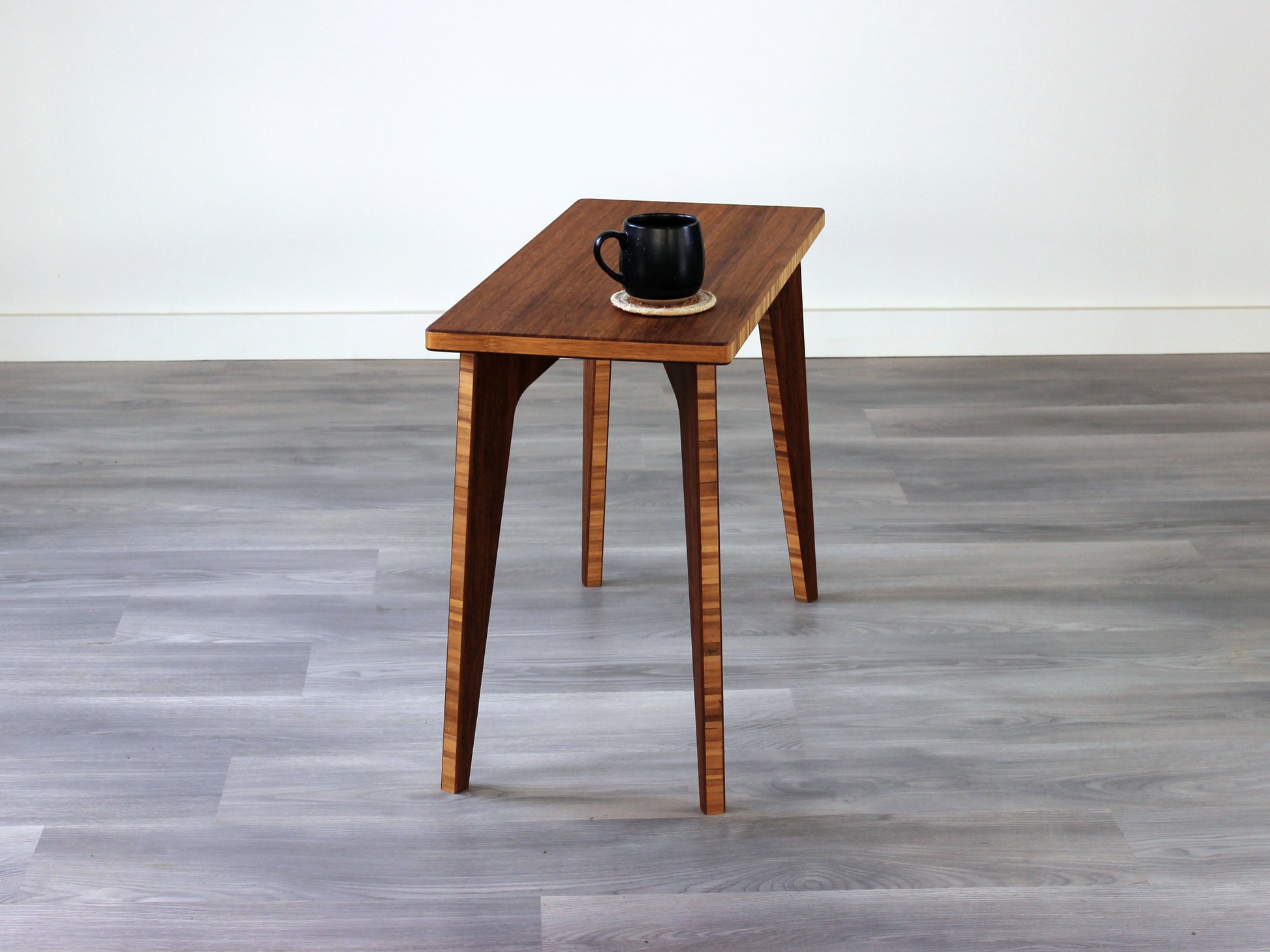A rectangular side table with a chestnut finish bamboo top and legs, placed on a grey floor, with a white background. Black cup on top of the table.
mid century
minimalist
chabudai
coffee table
side table