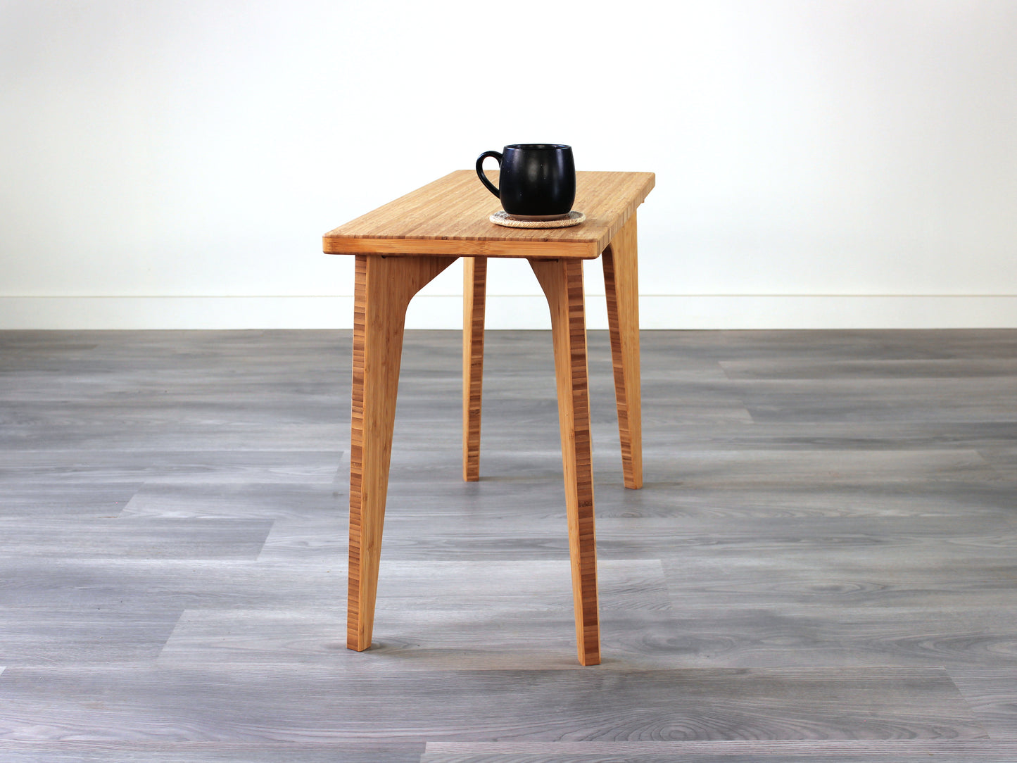 A rectangular side table with a natural finish bamboo top and legs, placed on a grey floor, with a white background. Black cup on top of the table.
mid century
minimalist
minimalist table
modern
coffee table
side table
