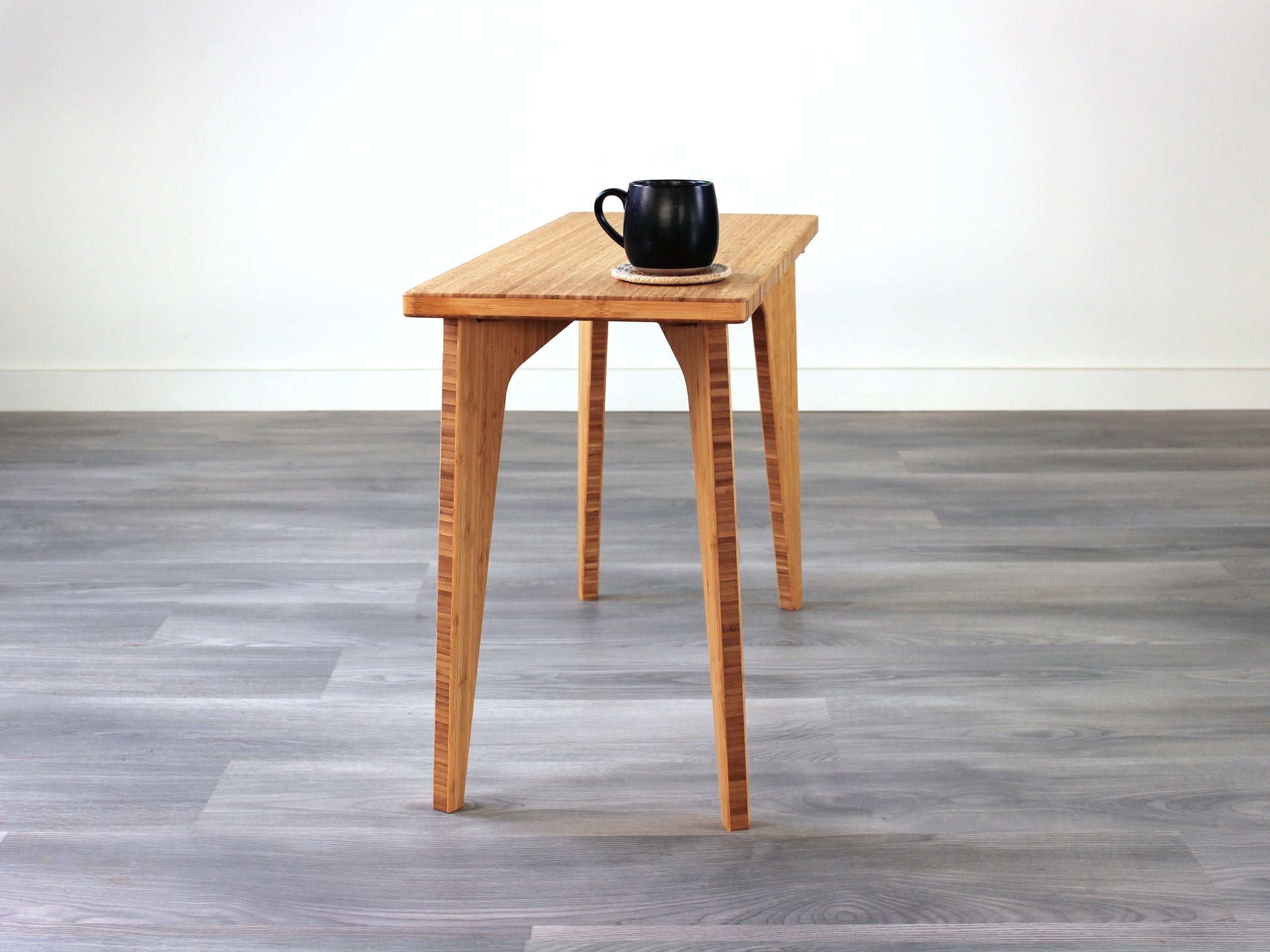 A rectangular side table with a natural finish bamboo top and legs, placed on a grey floor, with a white background. Black cup on top of the table.
mid century
minimalist
minimalist table
modern
coffee table
side table
