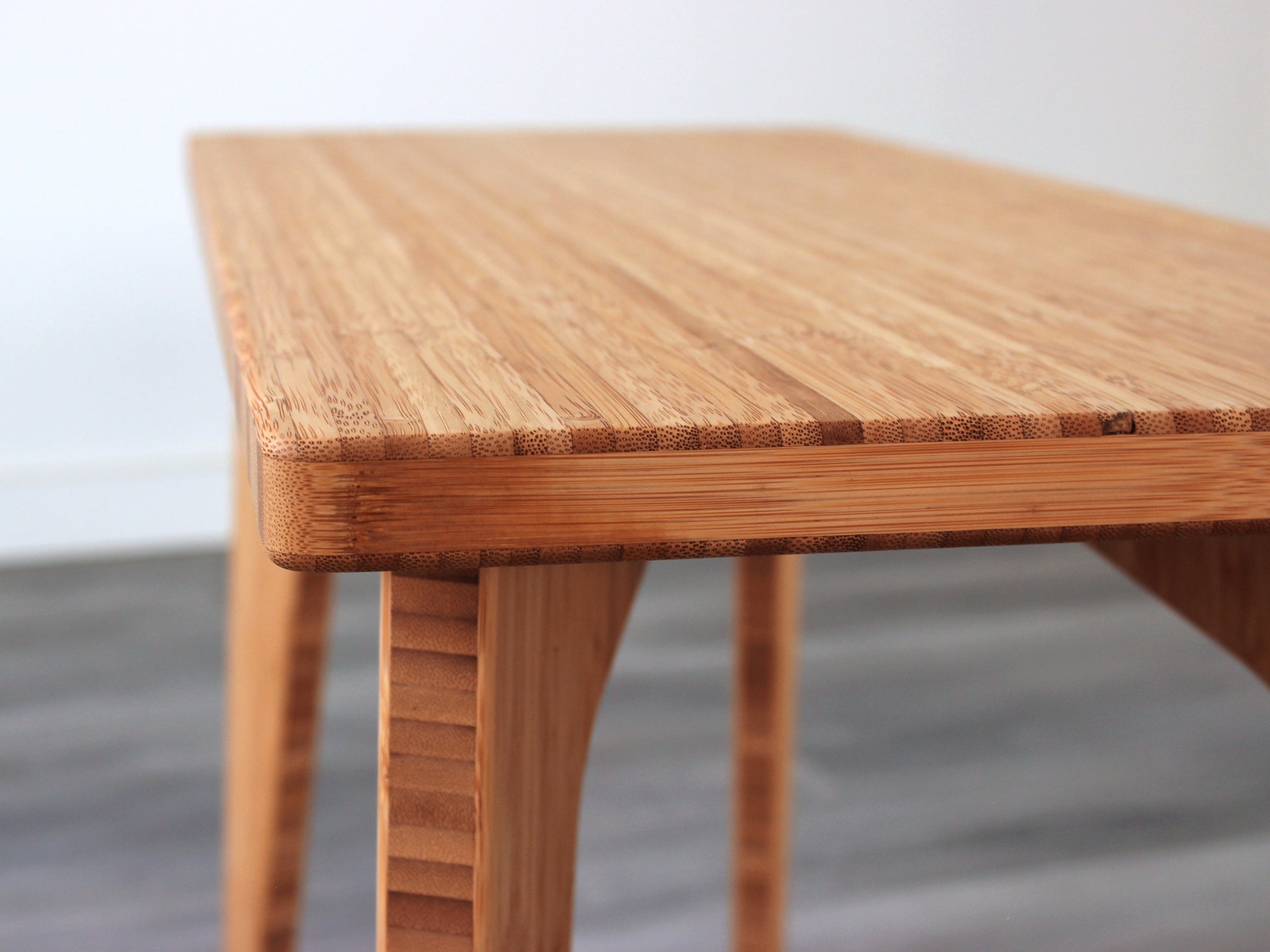 A rectangular side table with a natural finish bamboo top and legs, placed on a grey floor, with a white background. 
mid century
minimalist
contemporary
coffee table
side table
