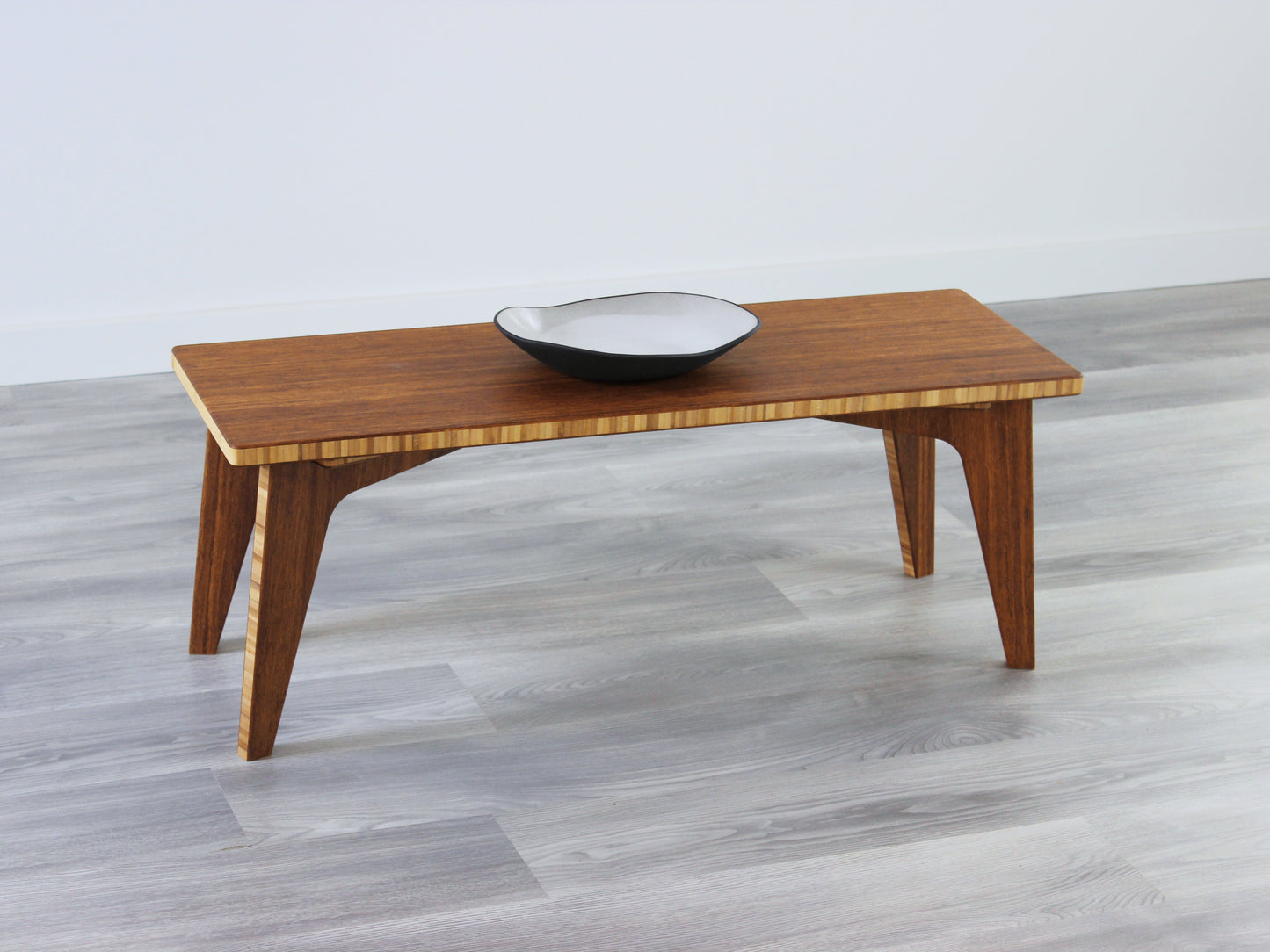 A small rectangular floor desk made of bamboo with a chestnut finish, featuring a single black piece of pottery on its top surface, placed on a grey floor with a white wall in the background.
japanese furniture
japanese low table
mid century
minimalist
minimalist table
