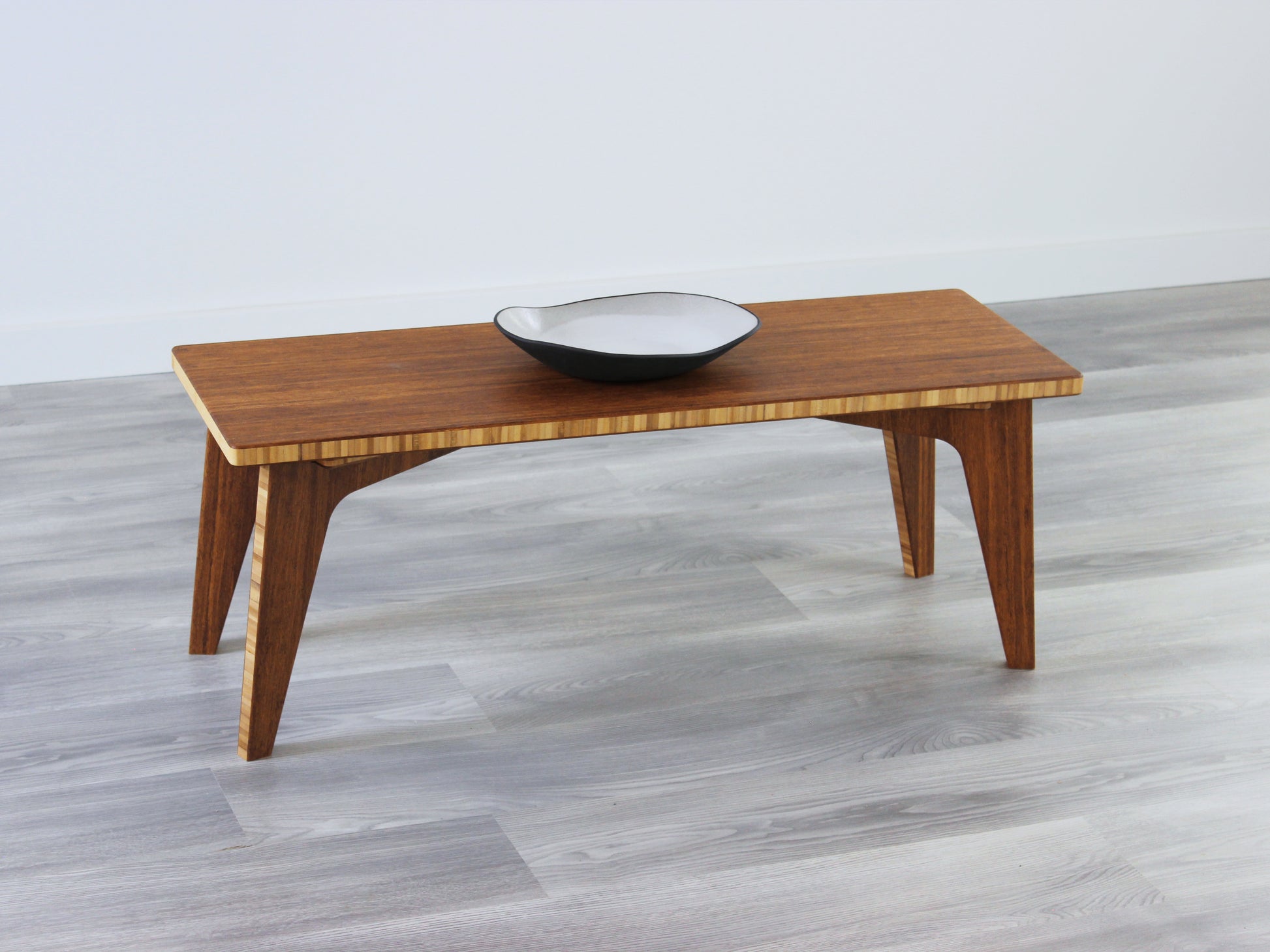 A small rectangular floor desk made of bamboo with a chestnut finish, featuring a single black piece of pottery on its top surface, placed on a grey floor with a white wall in the background.
japanese furniture
japanese low table
mid century
minimalist
minimalist table
