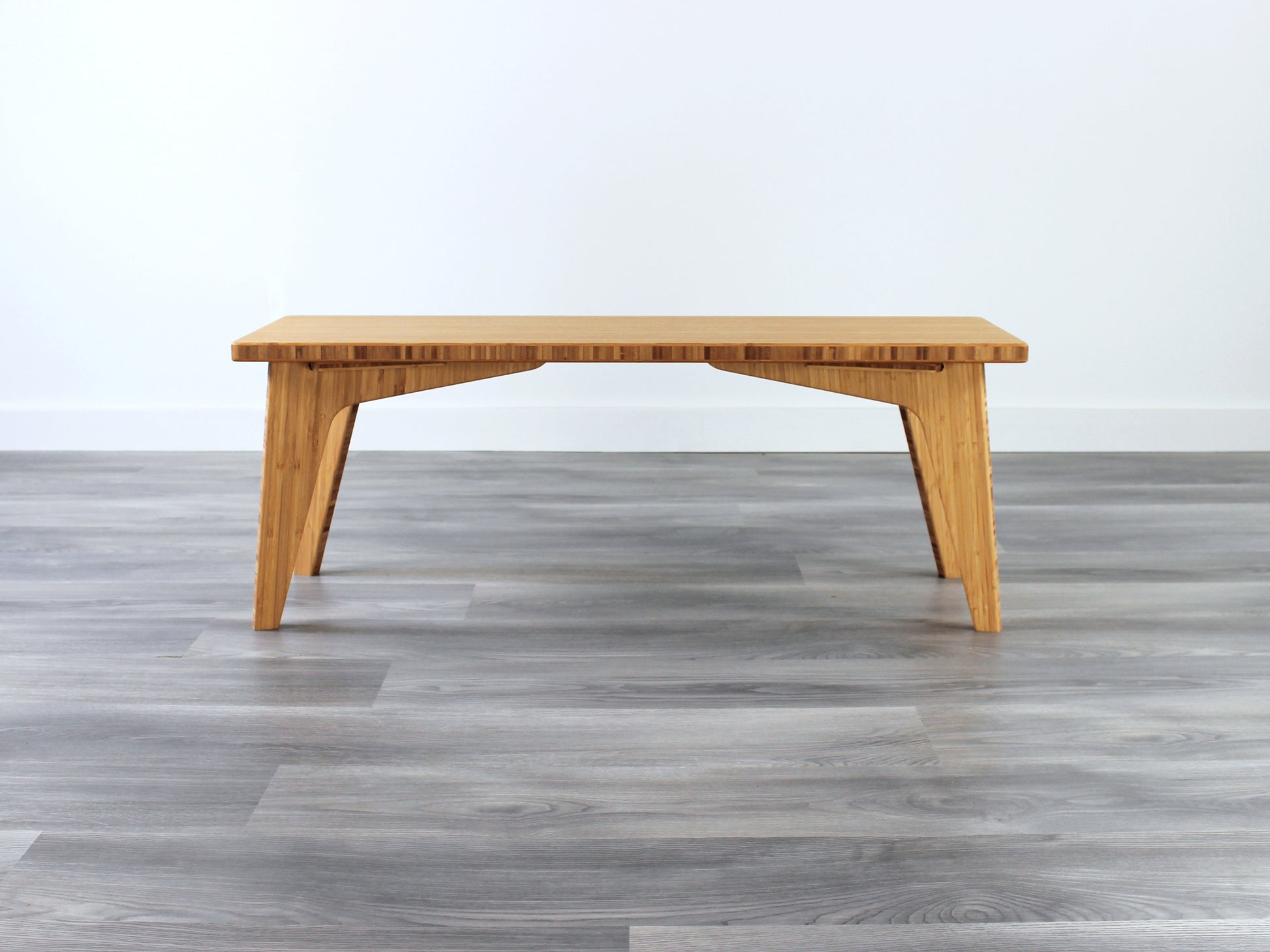 A small rectangular floor desk made of bamboo with a natural finish,  placed on a grey floor with a white wall in the background.
japanese furniture
japanese low table
mid century
minimalist
minimalist table
low desk 
