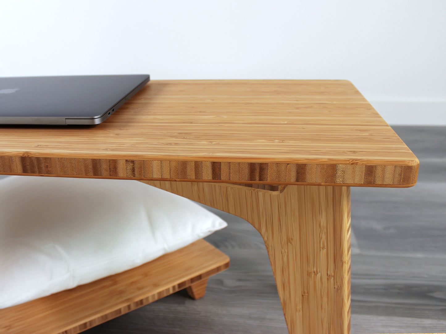 A close up side view of a small rectangular floor desk made of bamboo with a natural finish, a laptop on the table face with a Floor Chair Posture set beneath. All placed on a grey floor with a white wall in the background.
japanese furniture
japanese low table
mid century
minimalist
minimalist table
low desk 
tatami