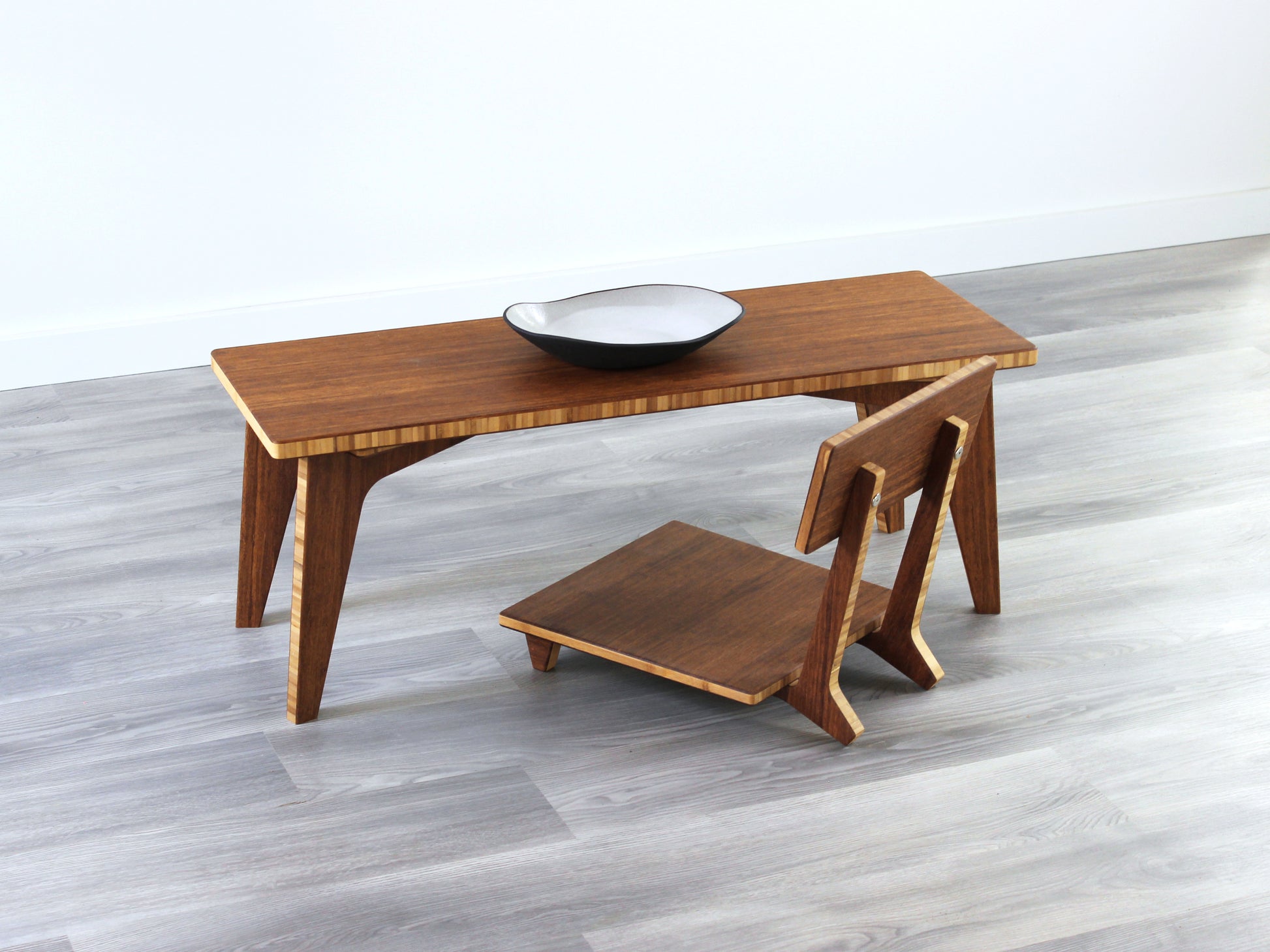 A small rectangular floor desk made of bamboo with a chestnut finish, featuring a single black piece of pottery on its top surface, placed on a grey floor with a white wall in the background. Floor Chair Comfort placed beneath.

mid century, minimalist, minimalist table, modern, square coffee table, table, tatami, Floor chair with back, posture support, low chair, chestnut bamboo