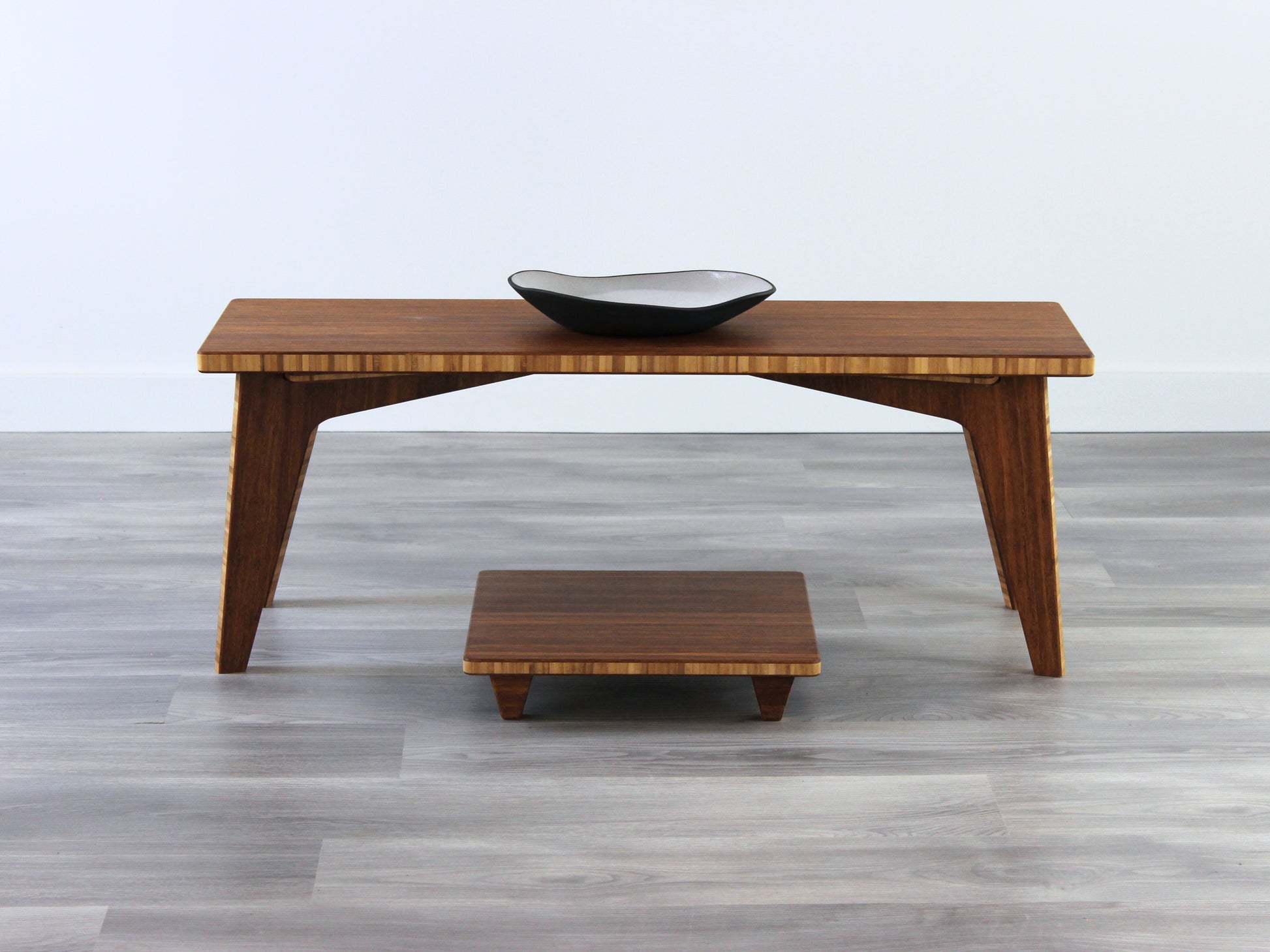 A small rectangular floor desk made of bamboo with a chestnut finish, featuring a single black piece of pottery on its top surface, placed on a grey floor with a white wall in the background. Floor Chair Posture placed beneath.

mid century, minimalist, minimalist table, modern, square coffee table, table, tatami, Floor chair, posture support, low chair, chestnut bamboo