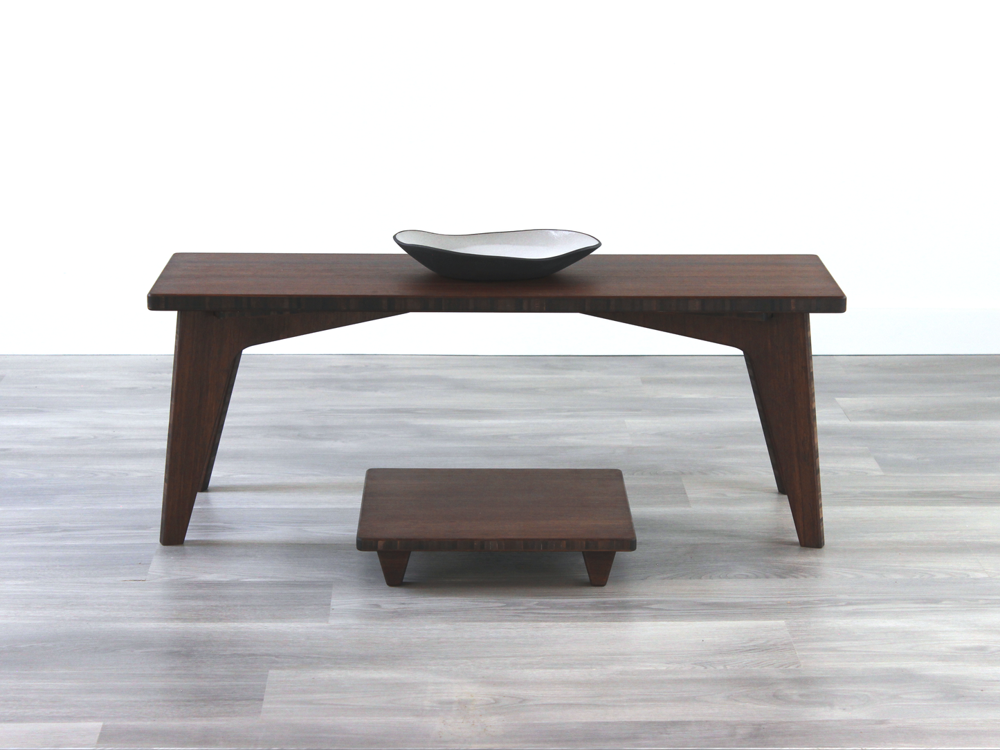 A small rectangular floor desk made of bamboo with a chestnut finish, featuring a single black piece of pottery on its top surface, placed on a grey floor with a white wall in the background. Floor Chair Posture placed beneath.


walnut bamboo coffee table, low chair with pillow, chabudai, tatami, japanese, mid-century, organic bowl on table
