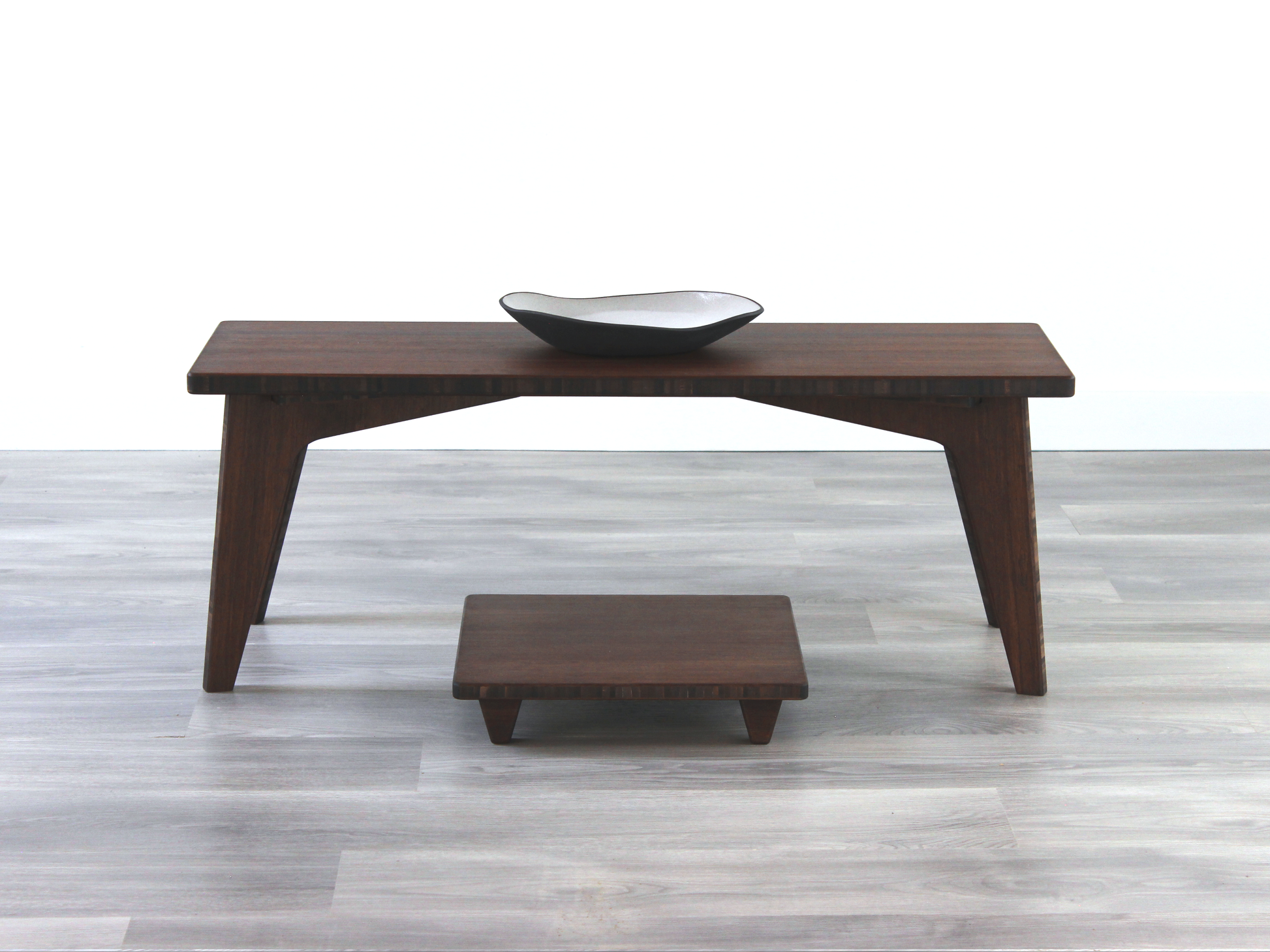 A small rectangular floor desk made of bamboo with a chestnut finish, featuring a single black piece of pottery on its top surface, placed on a grey floor with a white wall in the background. Floor Chair Posture placed beneath.


walnut bamboo coffee table, low chair with pillow, chabudai, tatami, japanese, mid-century, organic bowl on table