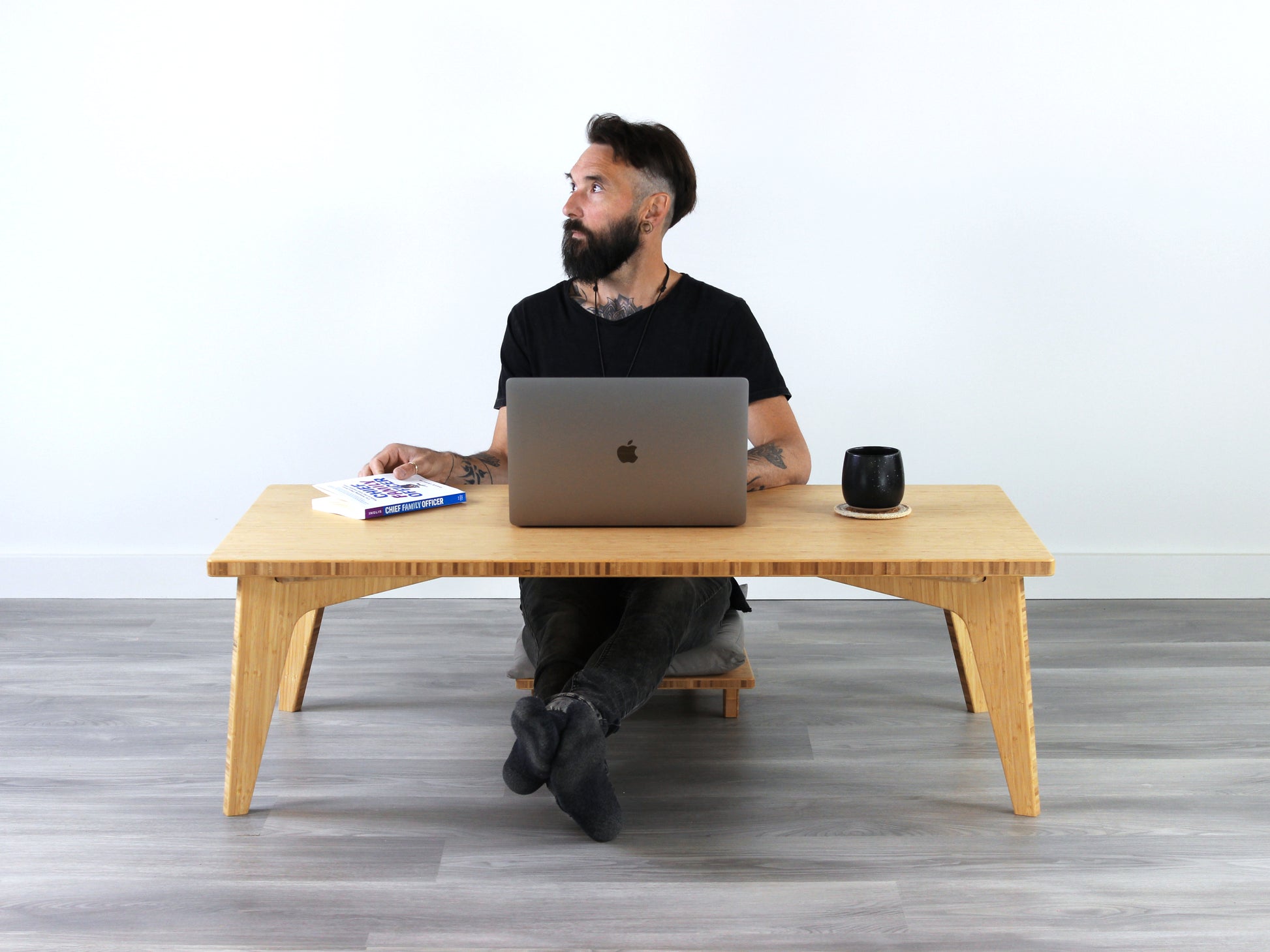 Small Rectangle Table Set - Natural, low table with Floor Chair Comfort set under with grey pillow. Person working on a laptop computer. Set on a grey floor, against a white background. A small black pottery vessel is on the table top. 

low table, coffee table, dining table, floor desk, floor chair, floor seating, low dining table, chabudai, tatami, kotatsu, minimalist, minimalist table,
modern
